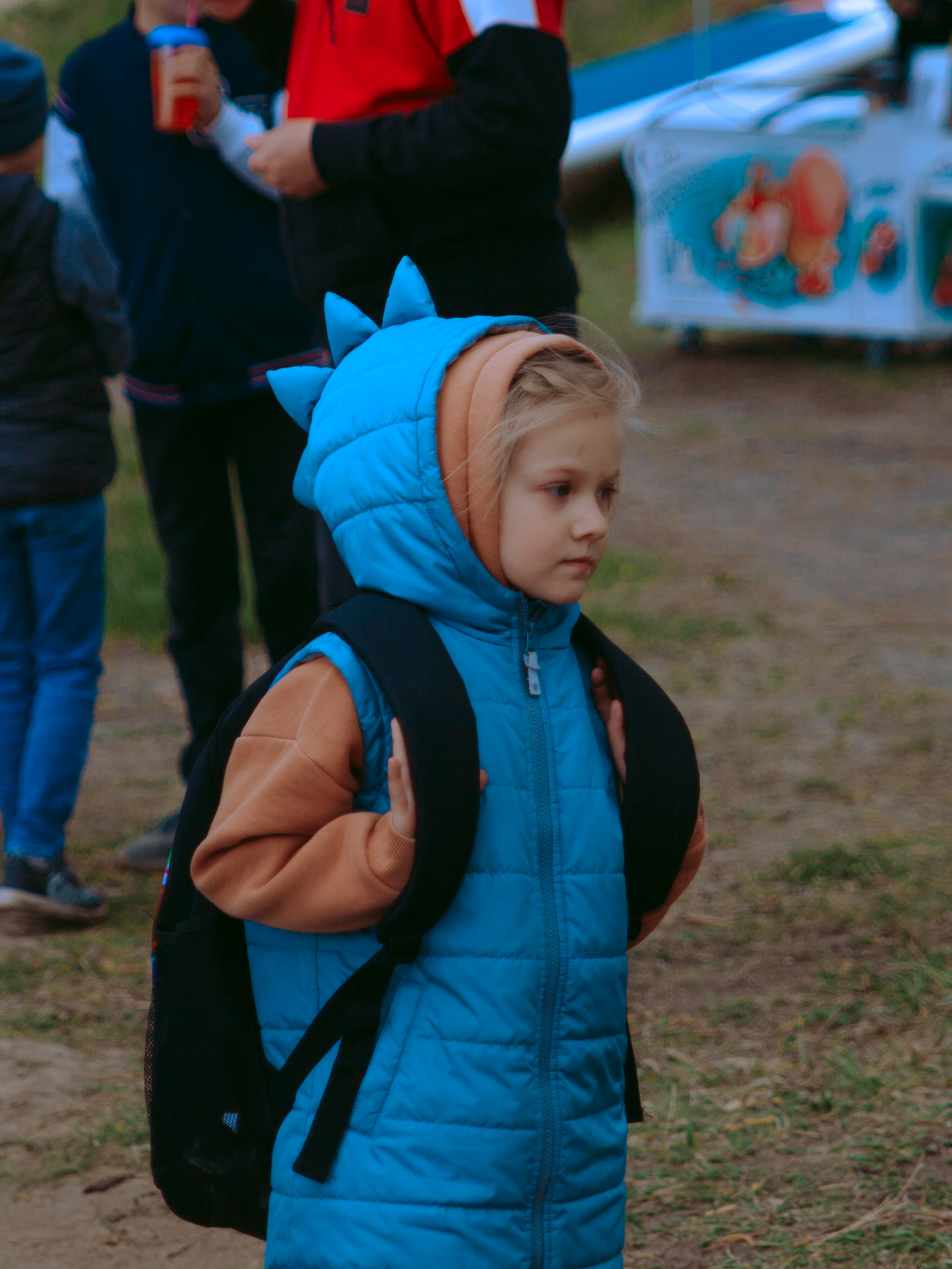 Ребенок в голубой куртке с фантазийным капюшоном динозаврик.