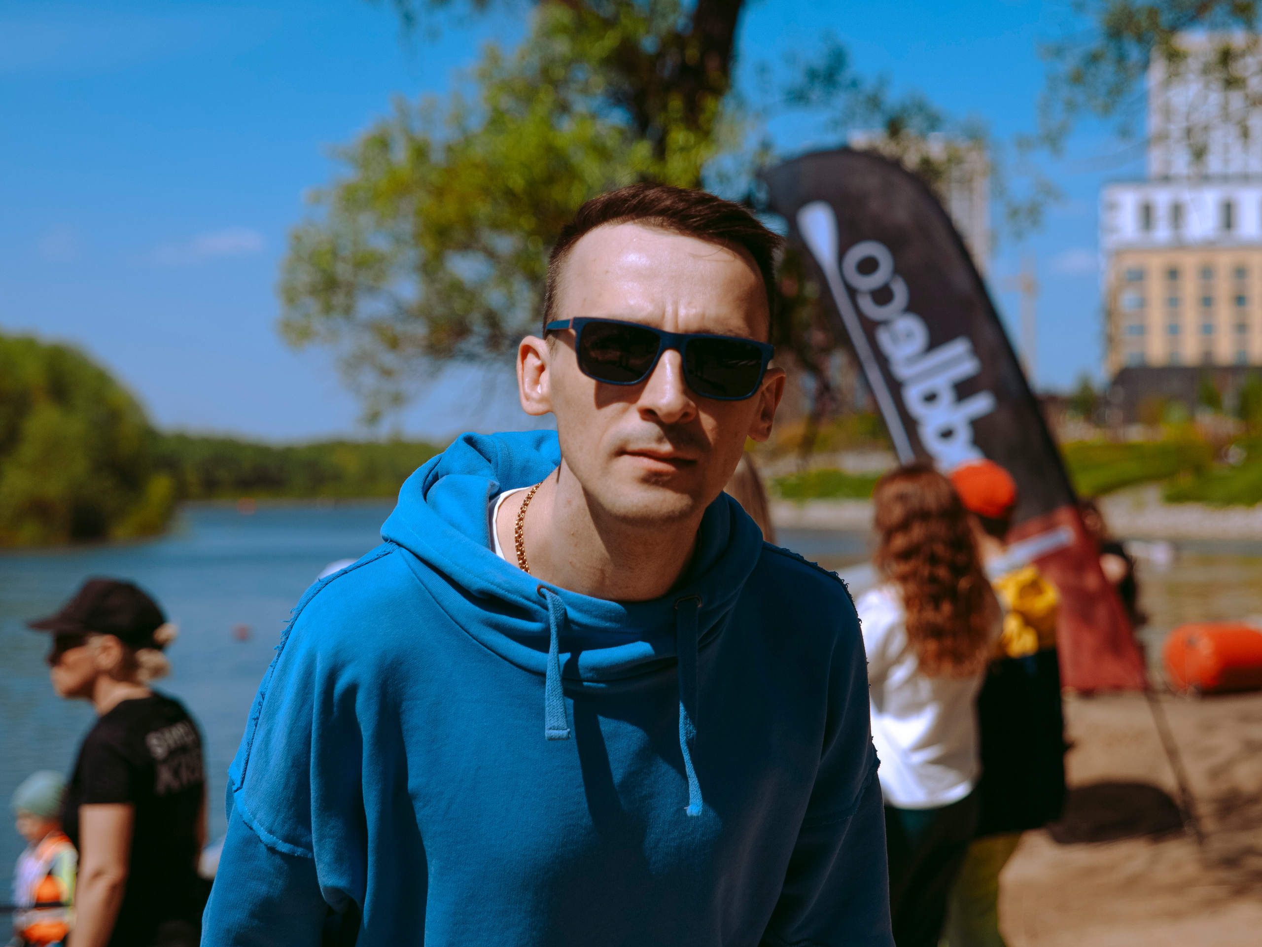 Мужчина в солнечных очках и синем худи смотрит в камеру.