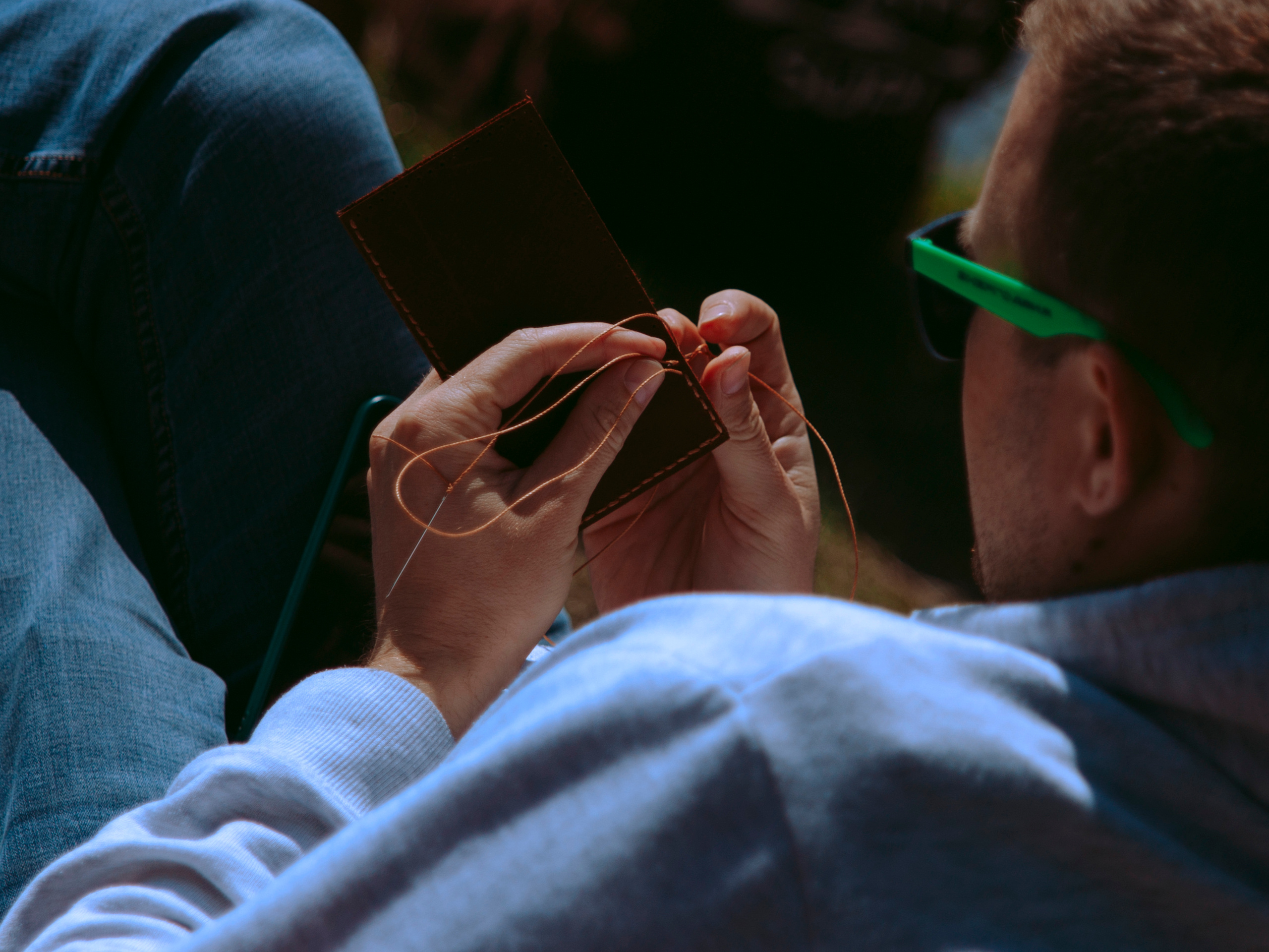 Мужчина шьет кожаный кошелек на свежем воздухе.