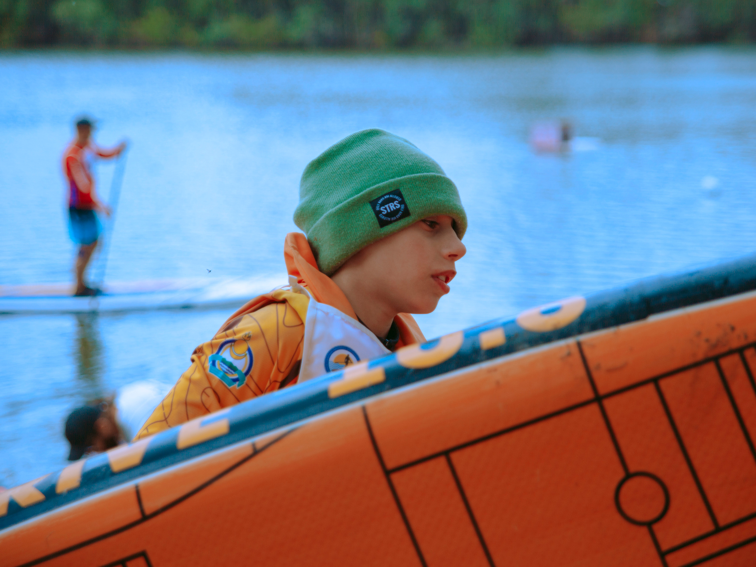 Мальчик в зеленой шапке несет оранжевый сап.