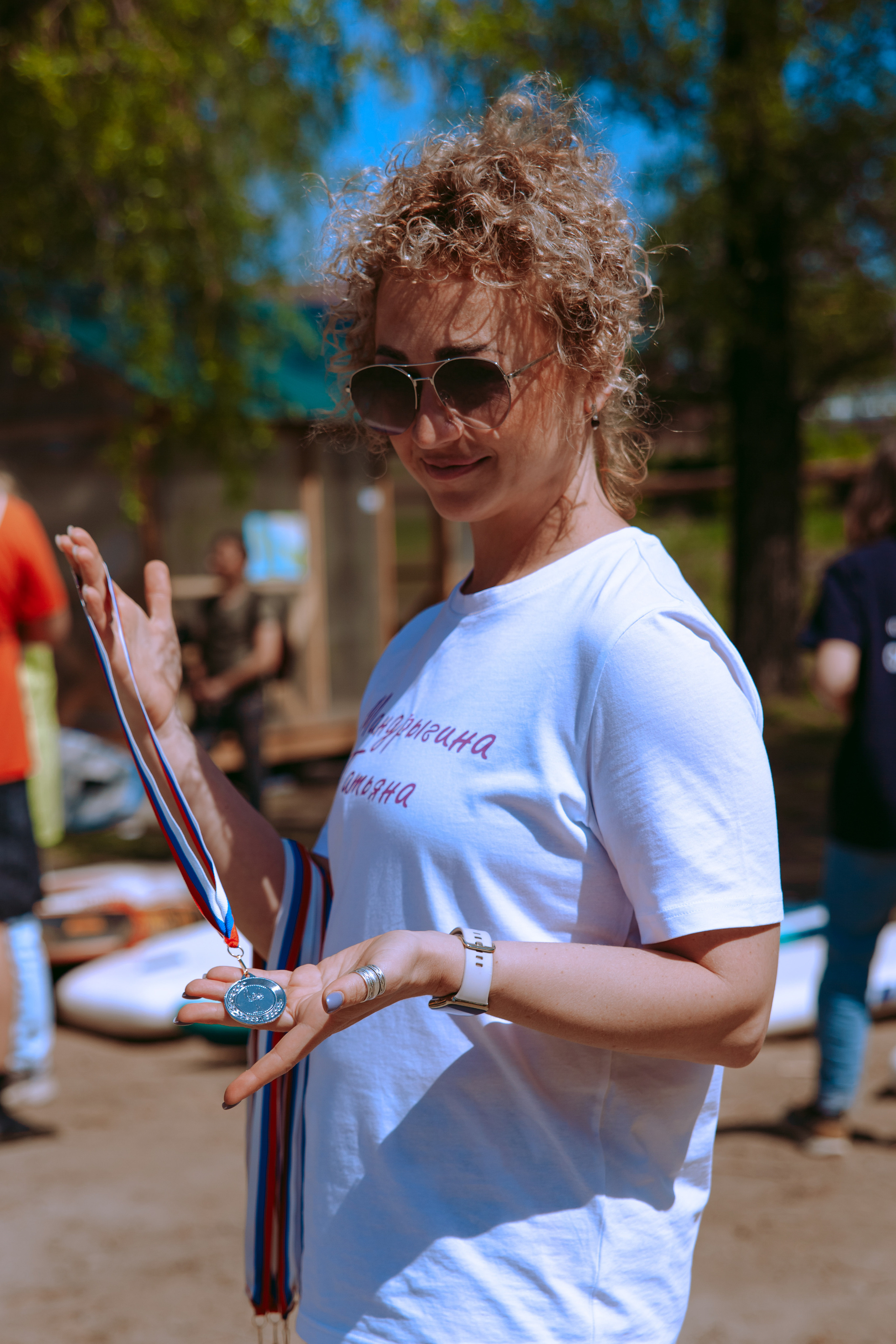 Кудрявая женщина кокетливо показывает медали.