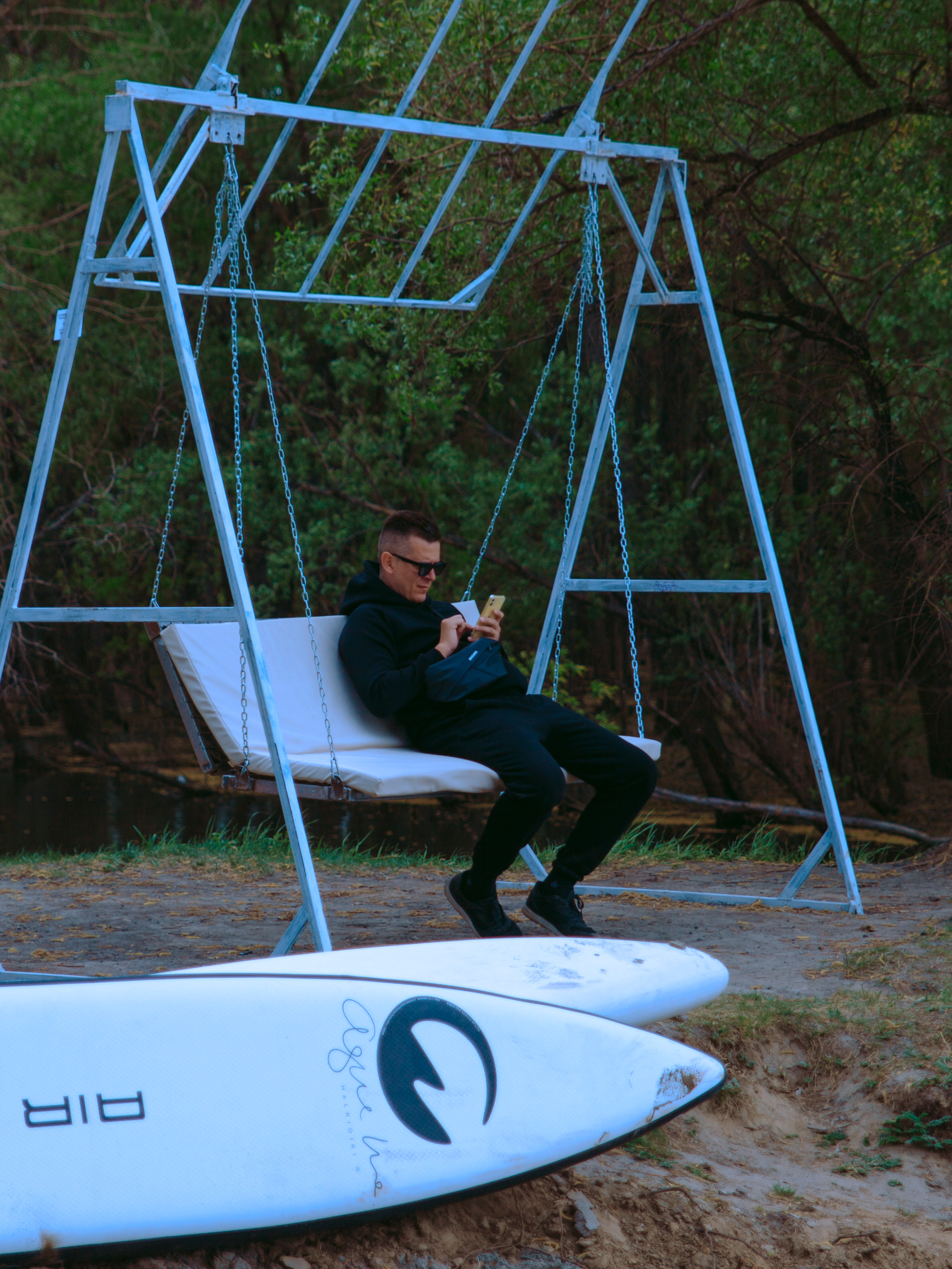 Мужчина сидит на качелях и смотрит в телефон.