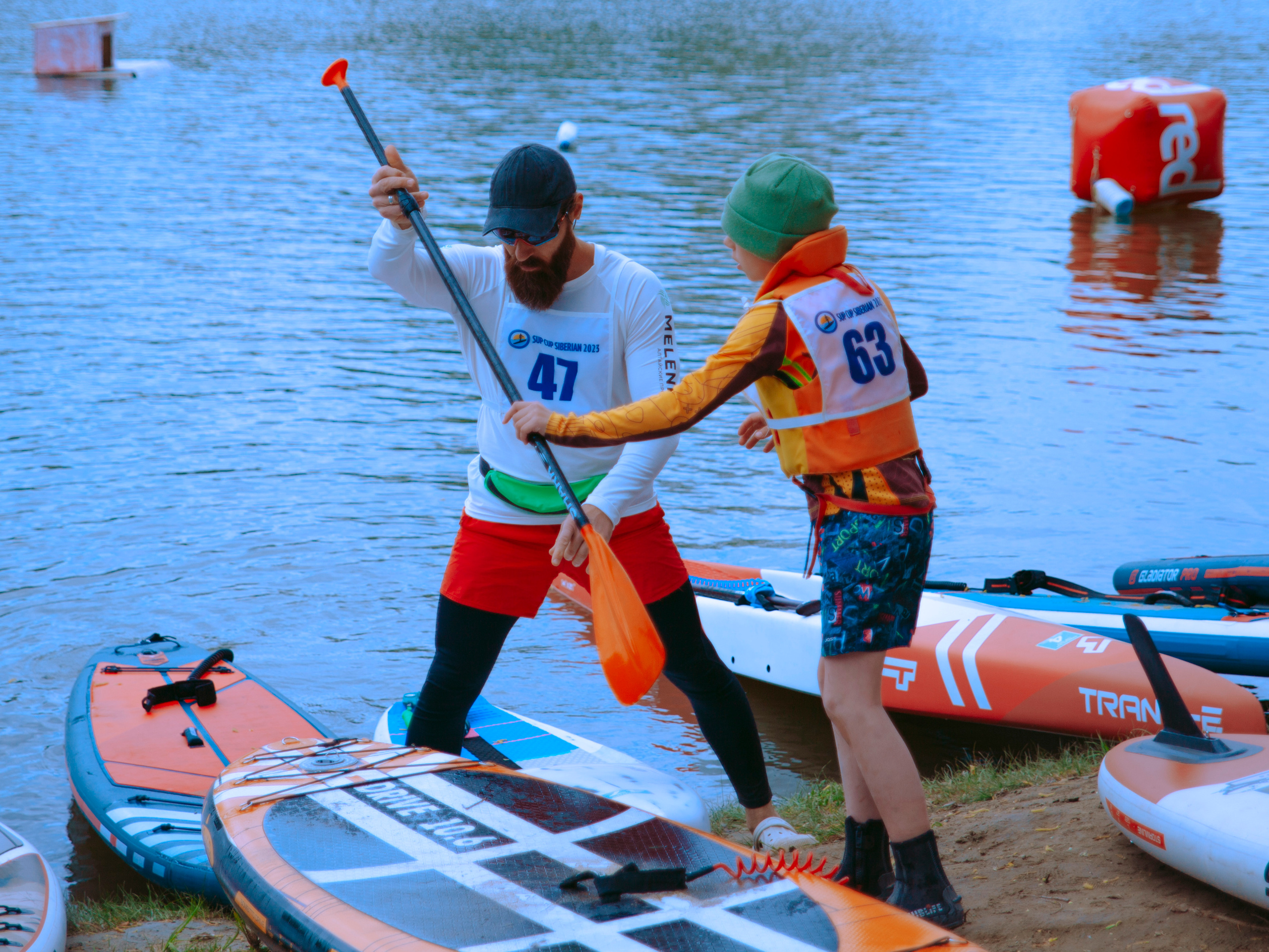Мужчина с бородой передает весло от сапа мальчику.