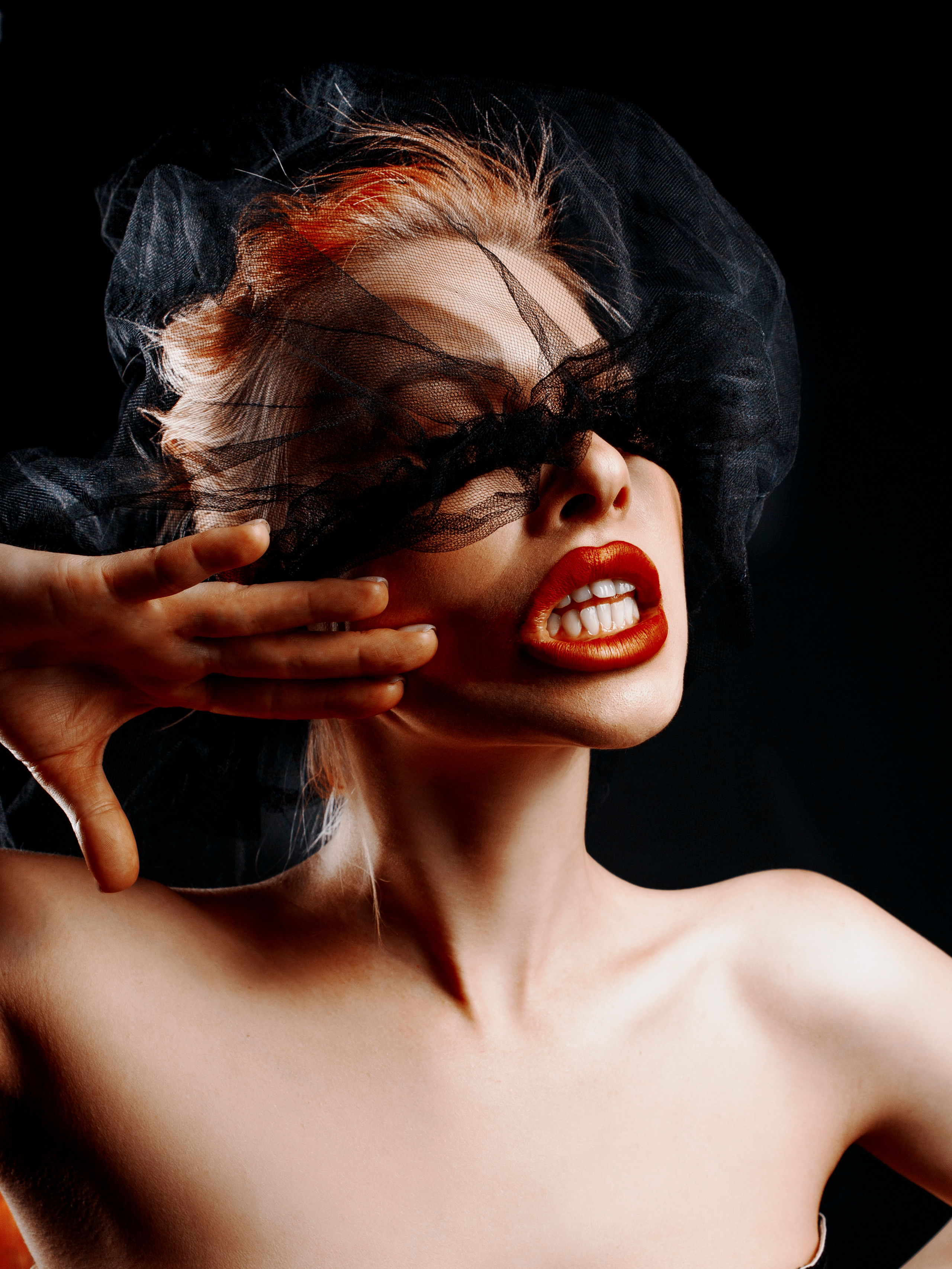 Девушка блондинка с черной вуалью агрессивно размазывает по лицу красную помаду.