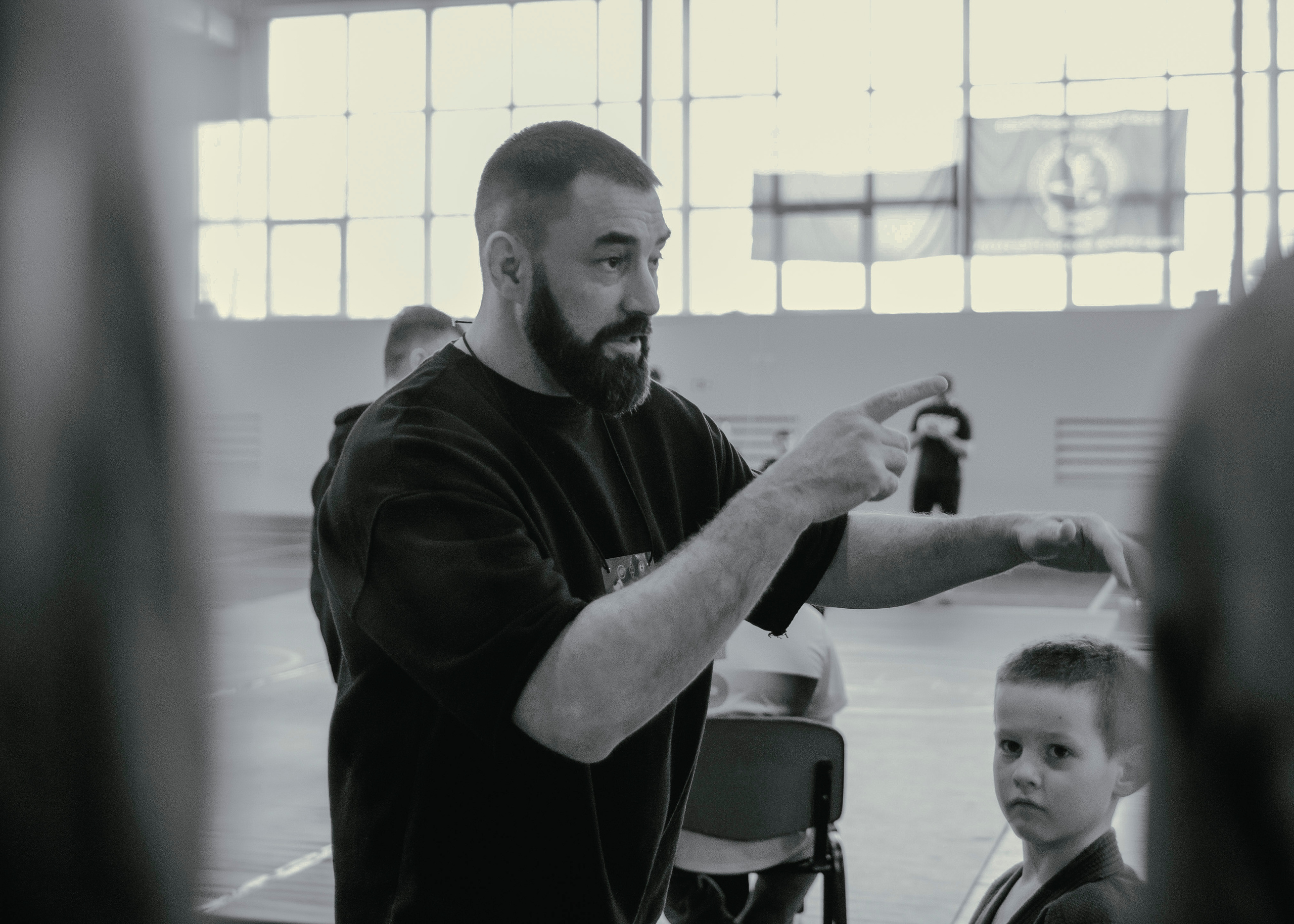 Мужественный тренер что-то уверенно говорит на детском турнире по джиу-джитсу.