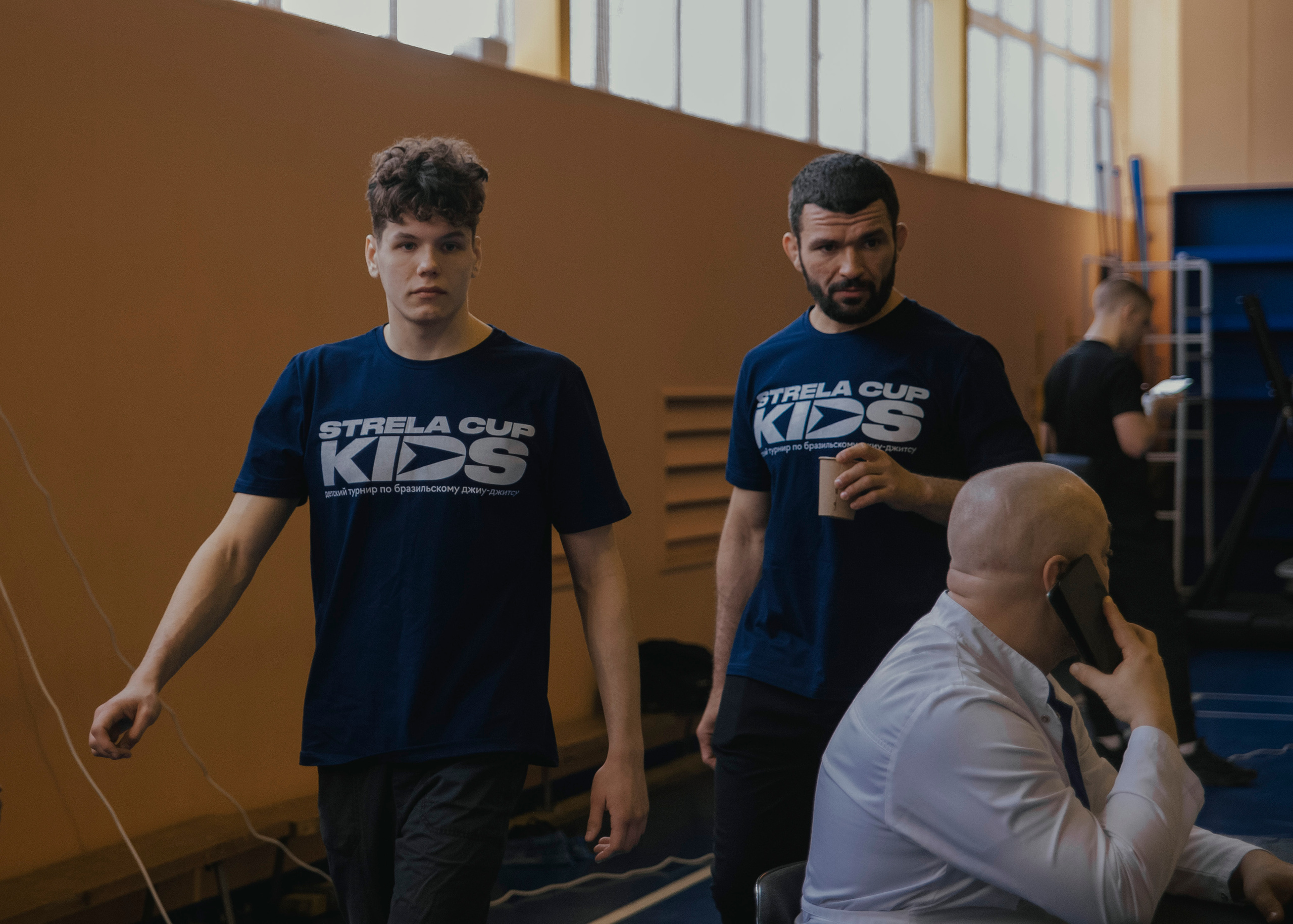 Два мужчины идут на детском турнире по джиу-джитсу.