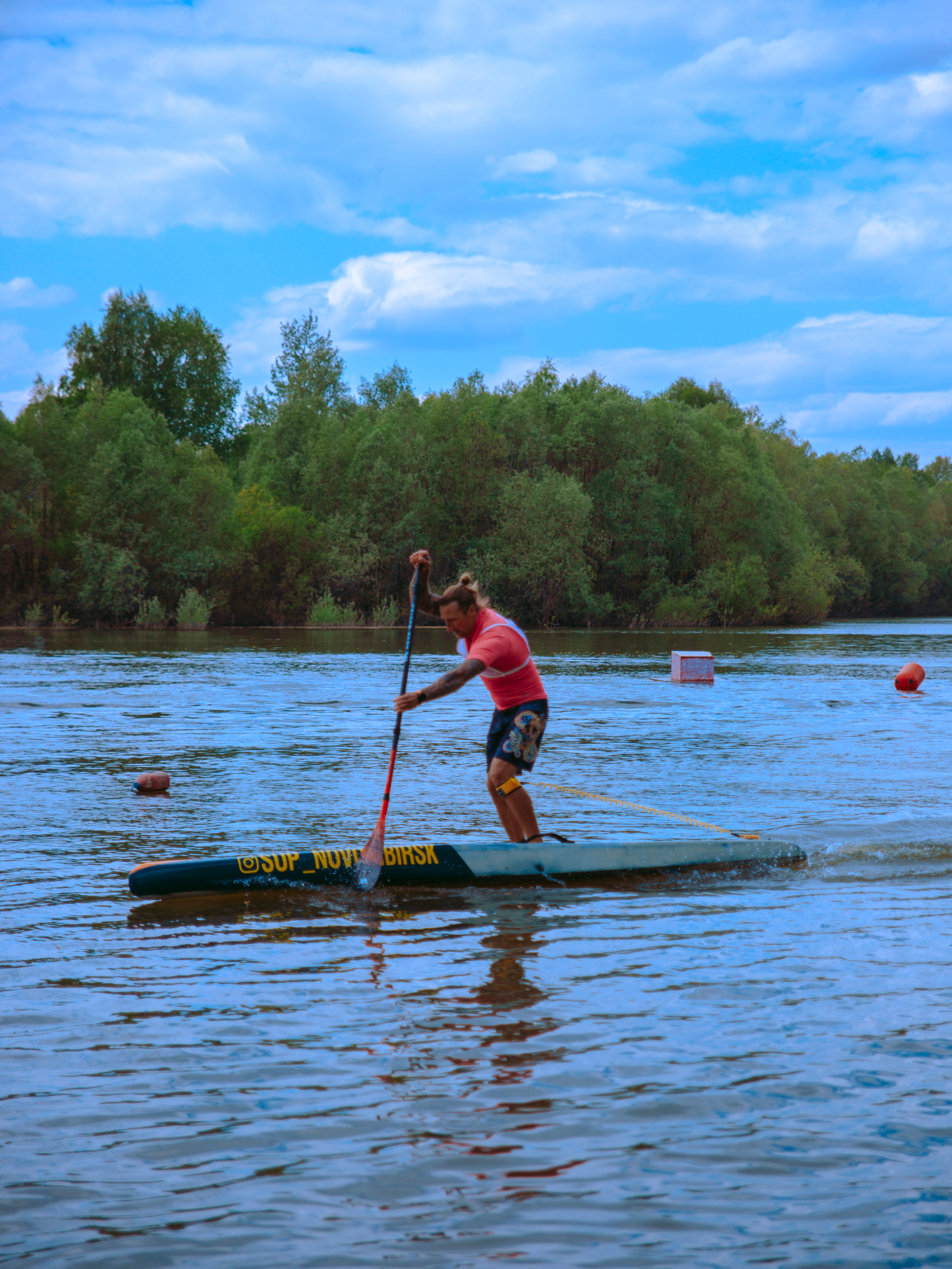 Мужчина с длинными волосами в розовой футболке плывет на сапе.