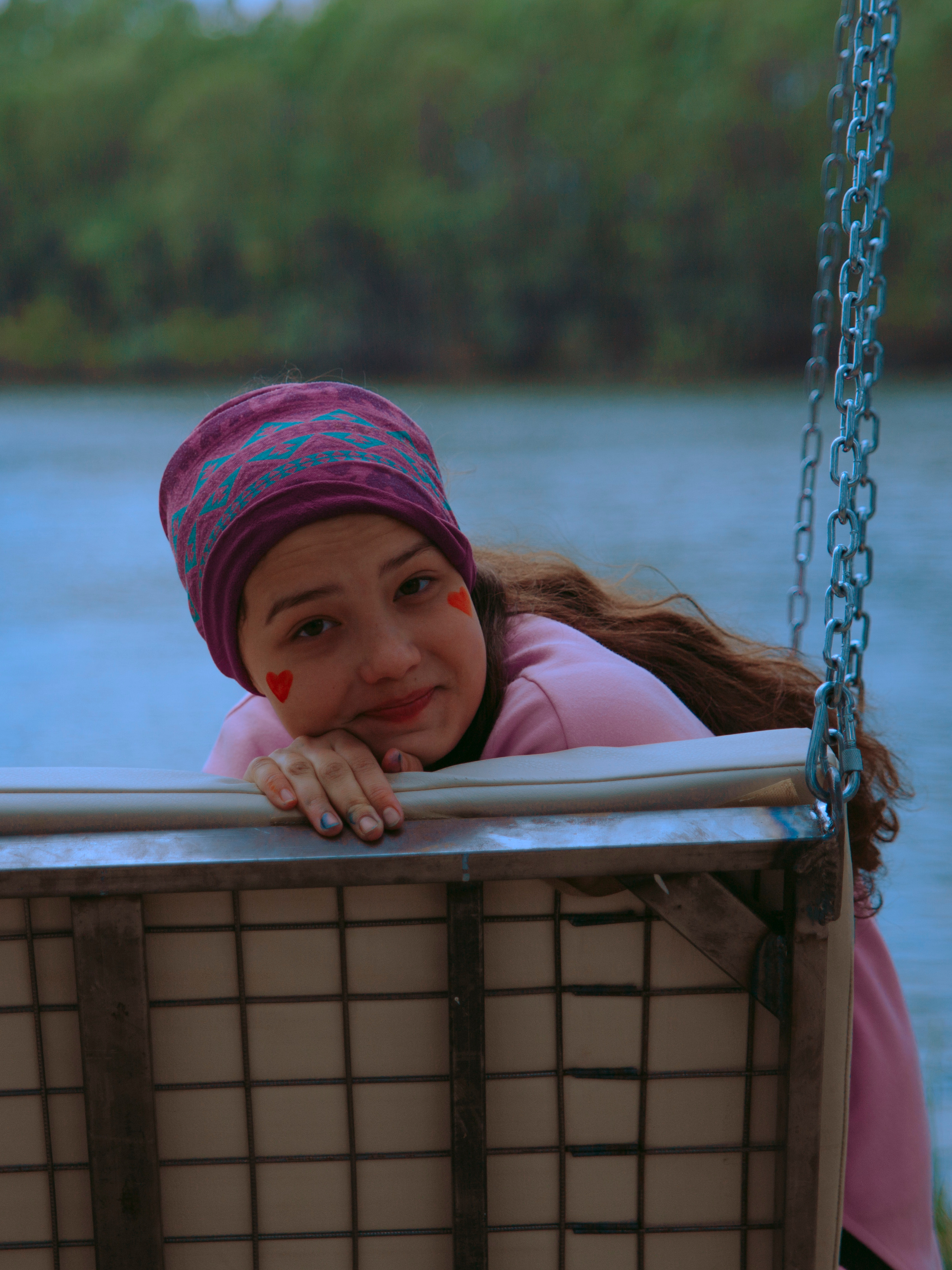 Девочка подросток сидит на качелях на фоне воды.