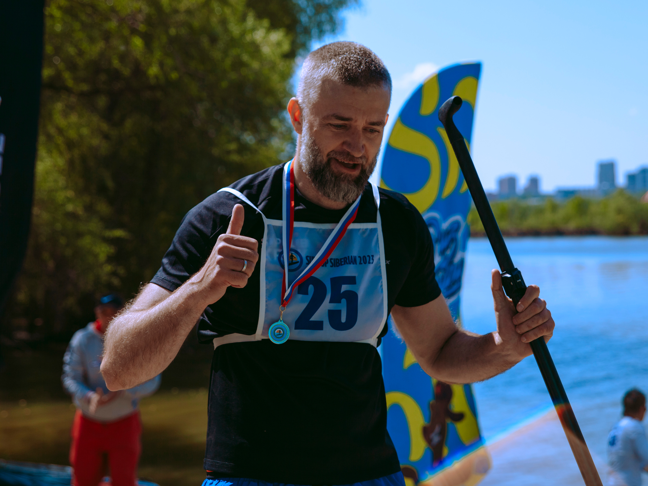 Мужчина спортсмен получает медаль и радуется победе, показывая большой палец.