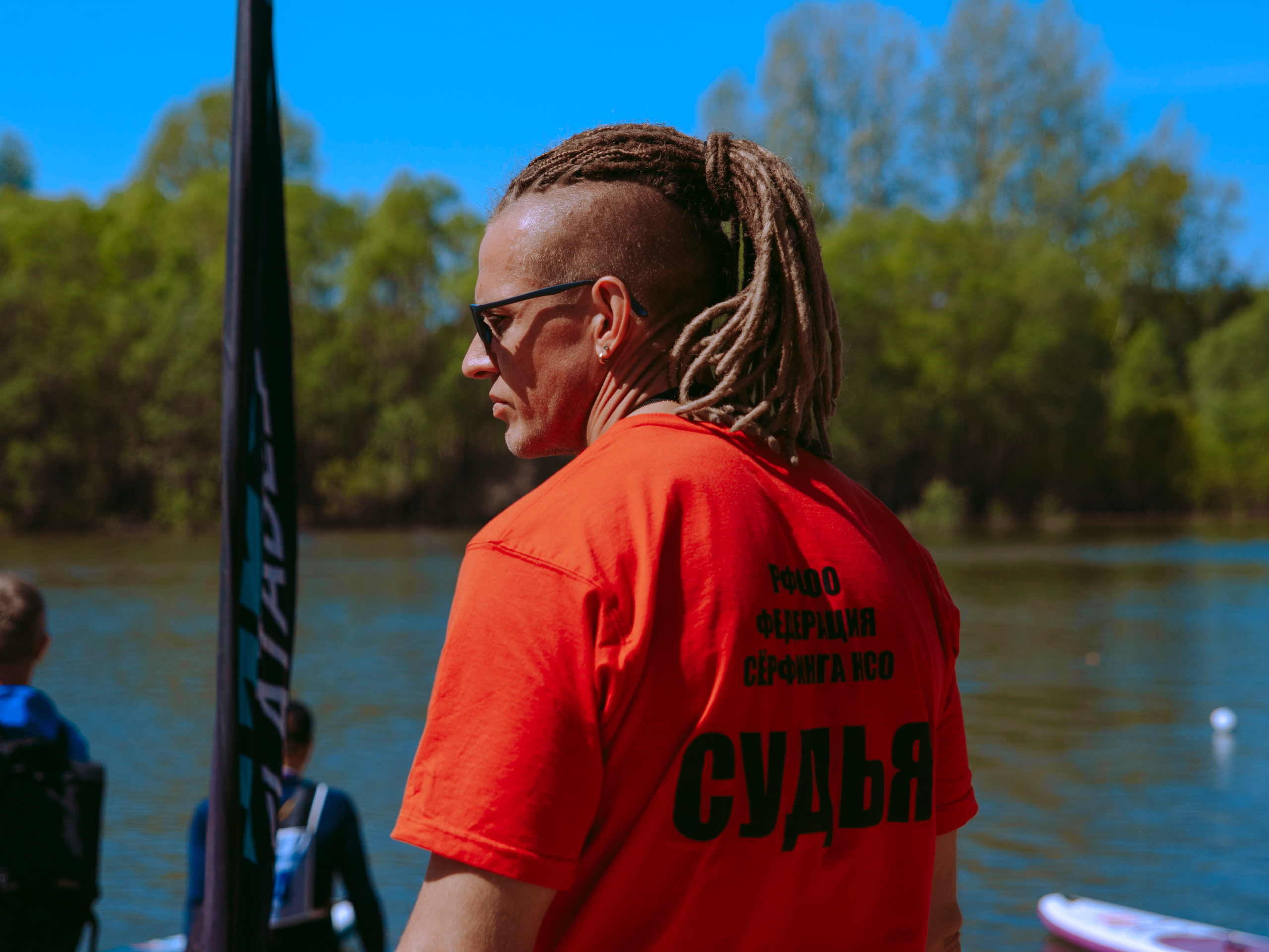 Мужчина судья с дредами в красной футболке и в солнечных очках.