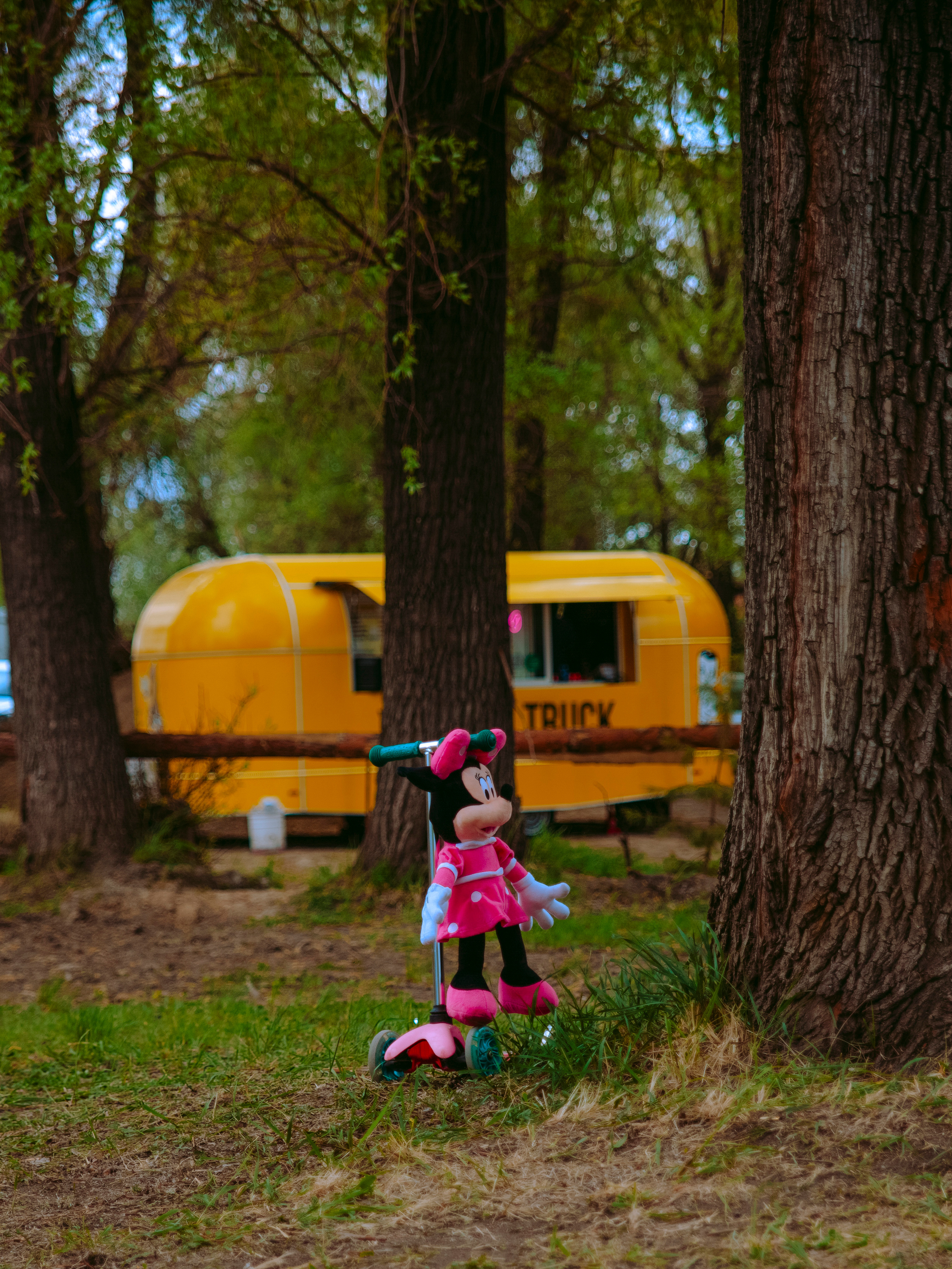 Самокат с розовым Микки-маусом минни-маус на фоне желтого фургончика в парке в лесу.