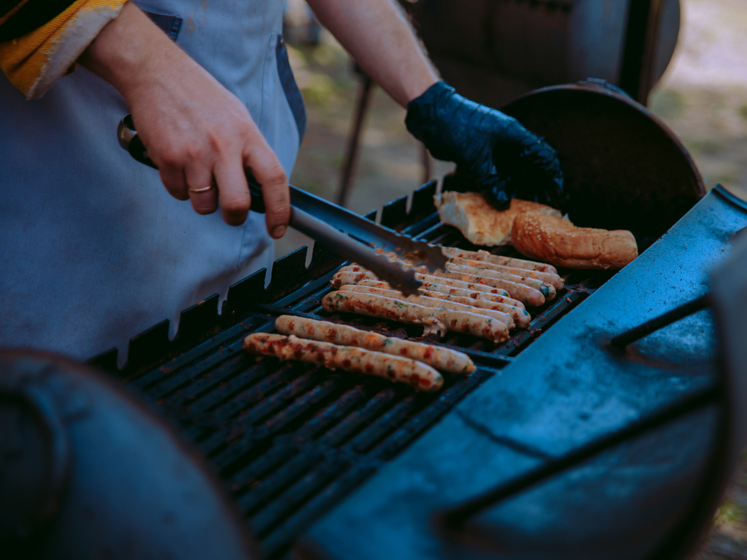Мужские руки жарят колбаски на мангале.