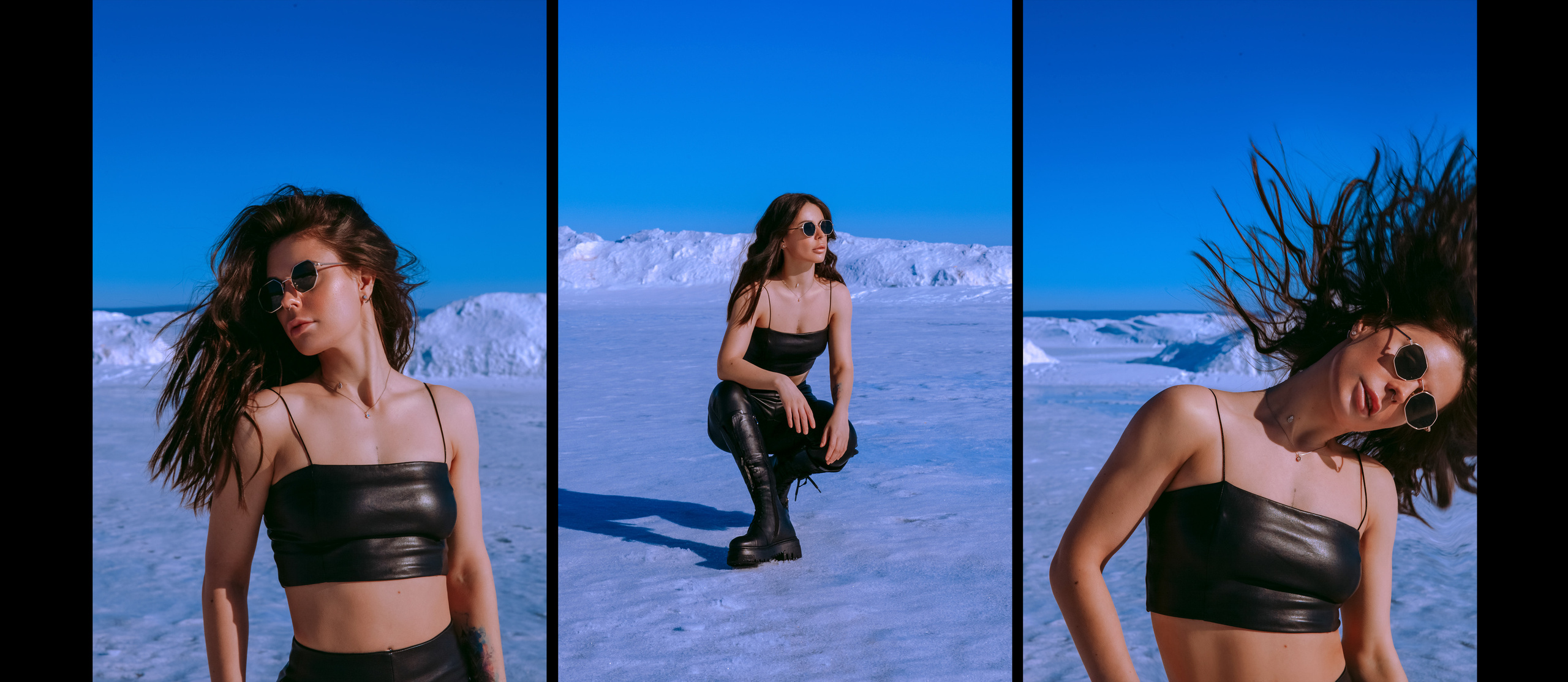 Девушка в черных солнечных очках и кожаном черном топе на фоне синего неба и белого снега машет волосами и сидит на корточках.