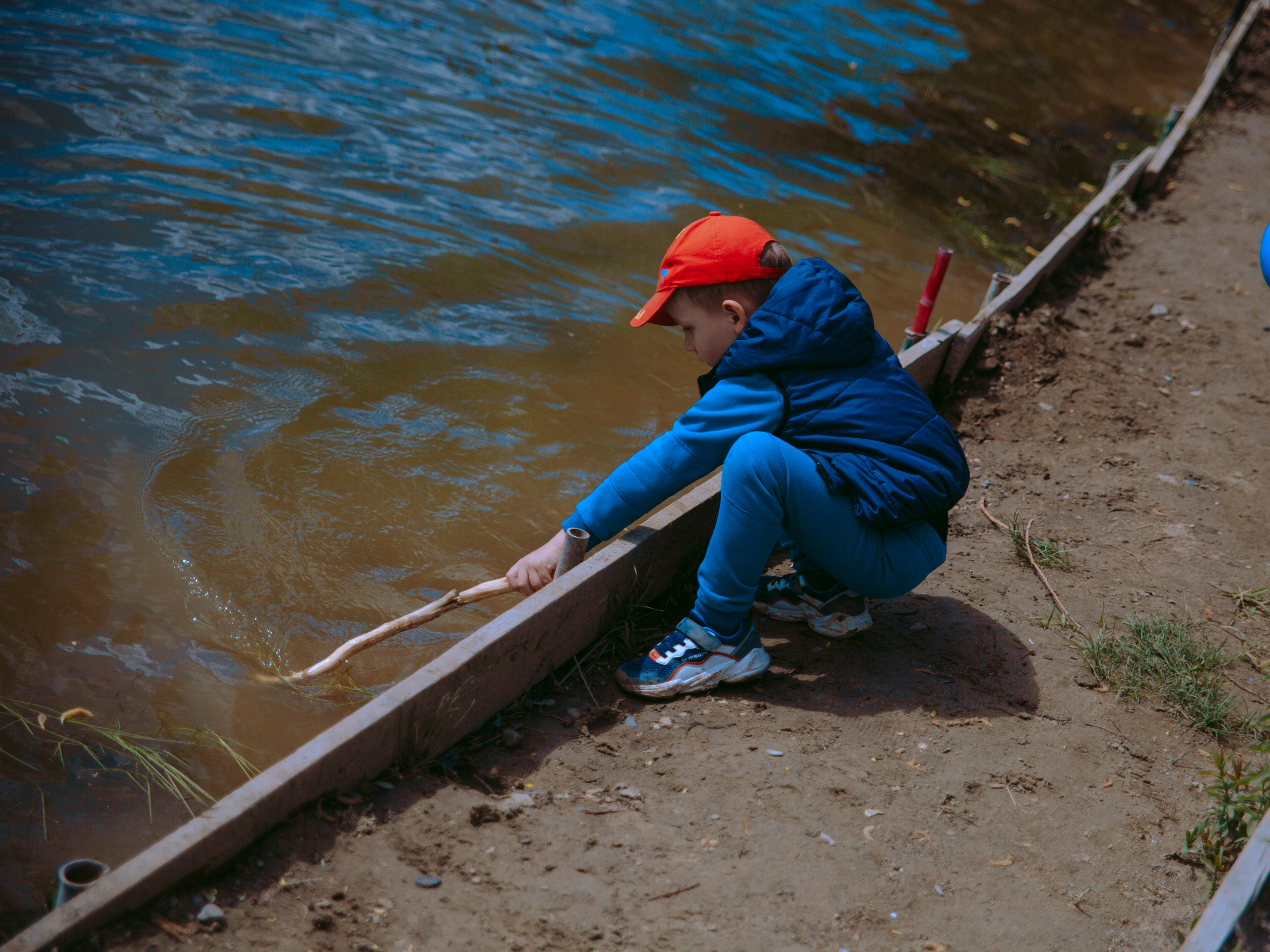 Мальчик водит палкой веткой по воде.