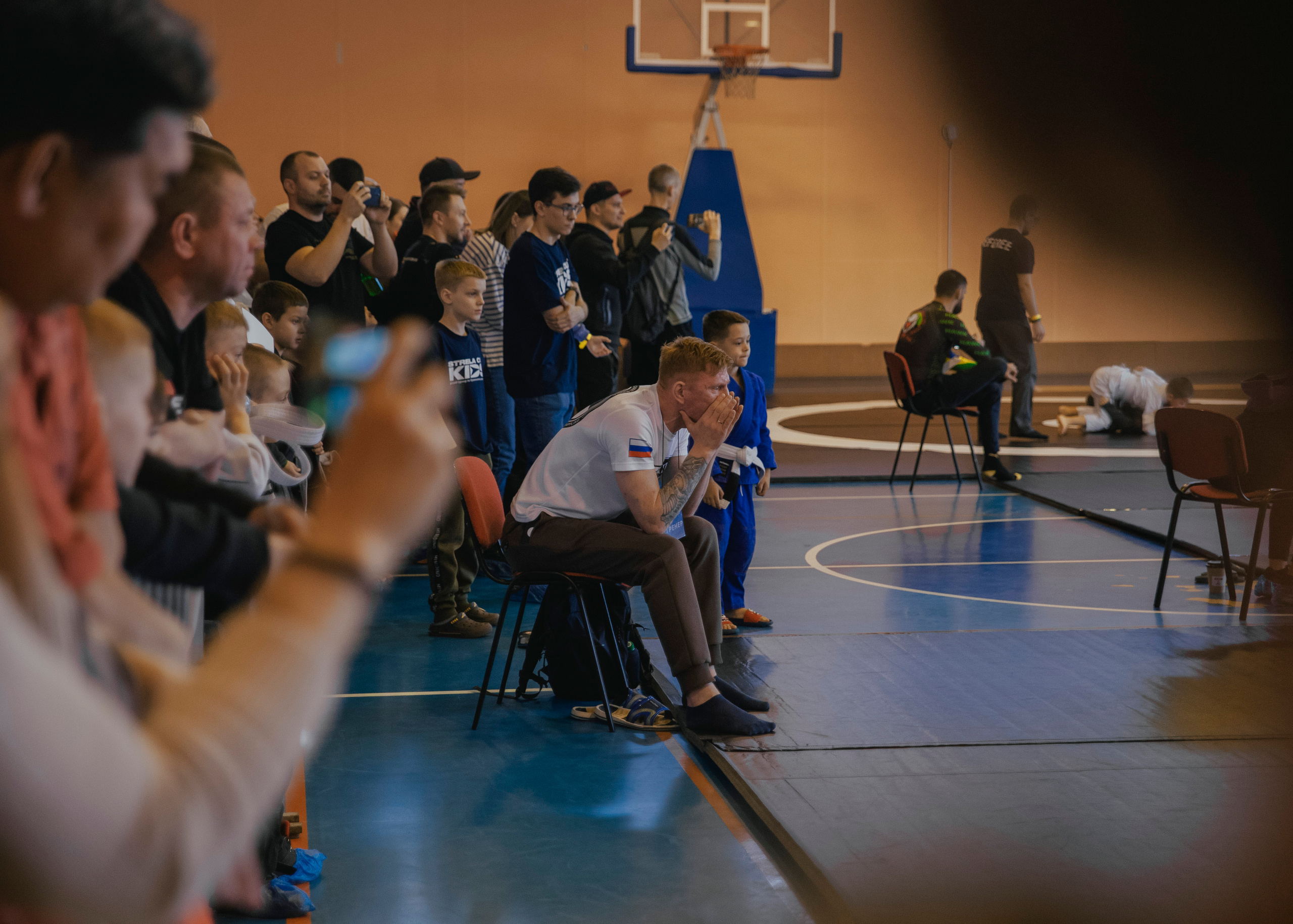 Тренер в толпе в углу ковра на спортивном турнире.