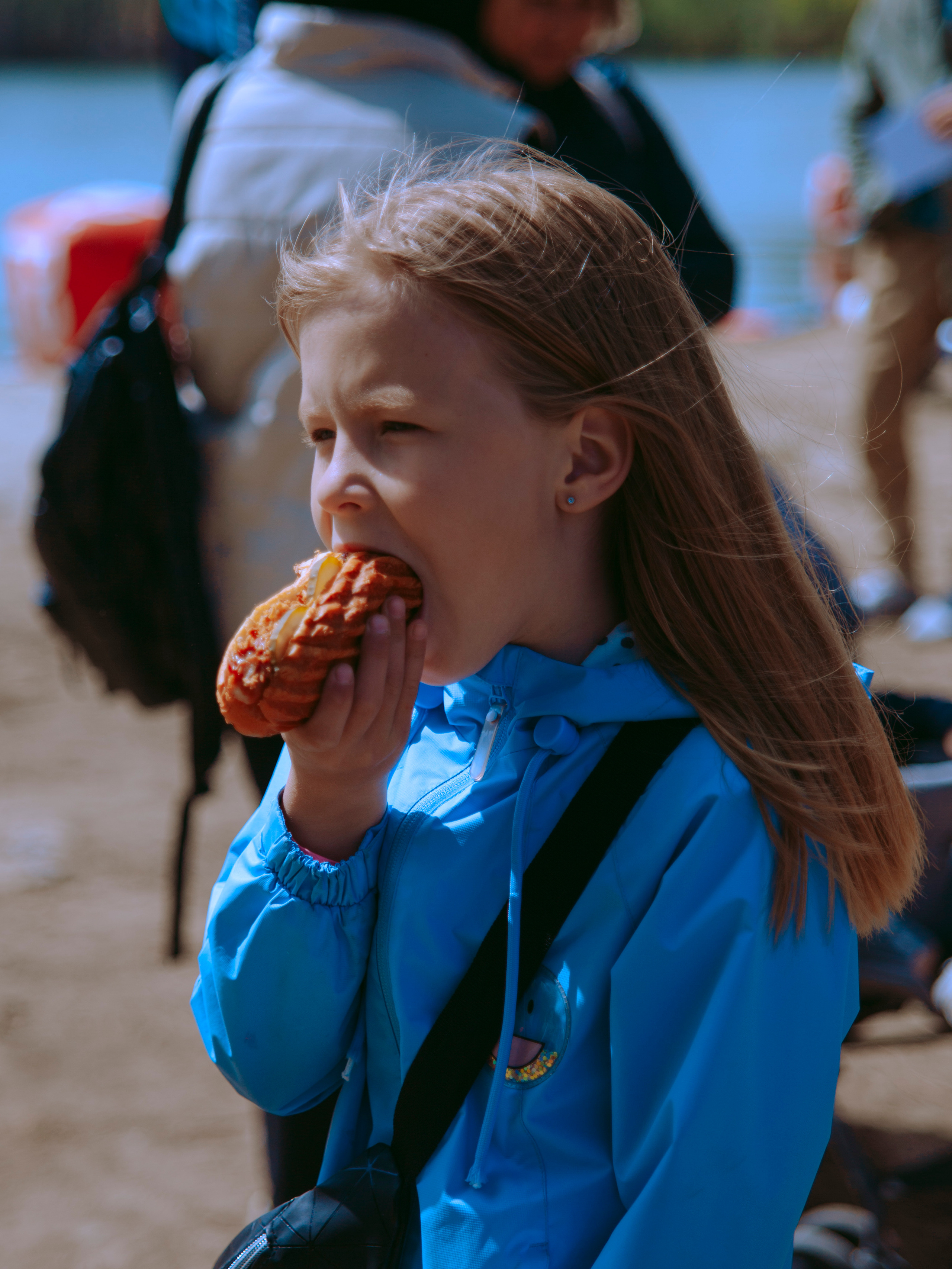 Маленькая девочка ест хот-дог, широко открыв рот.