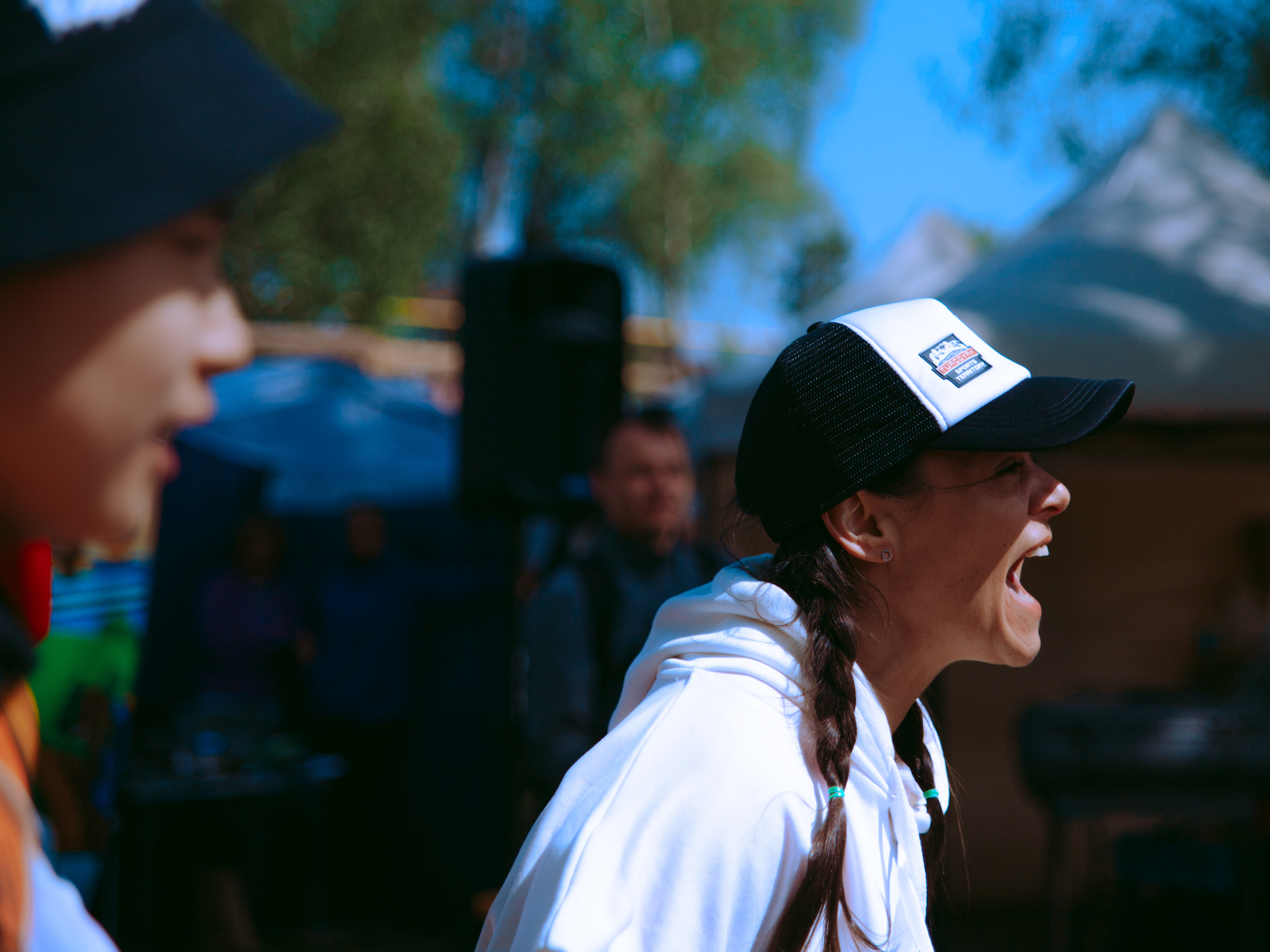 Девушка с косичками и в кепке кричит.