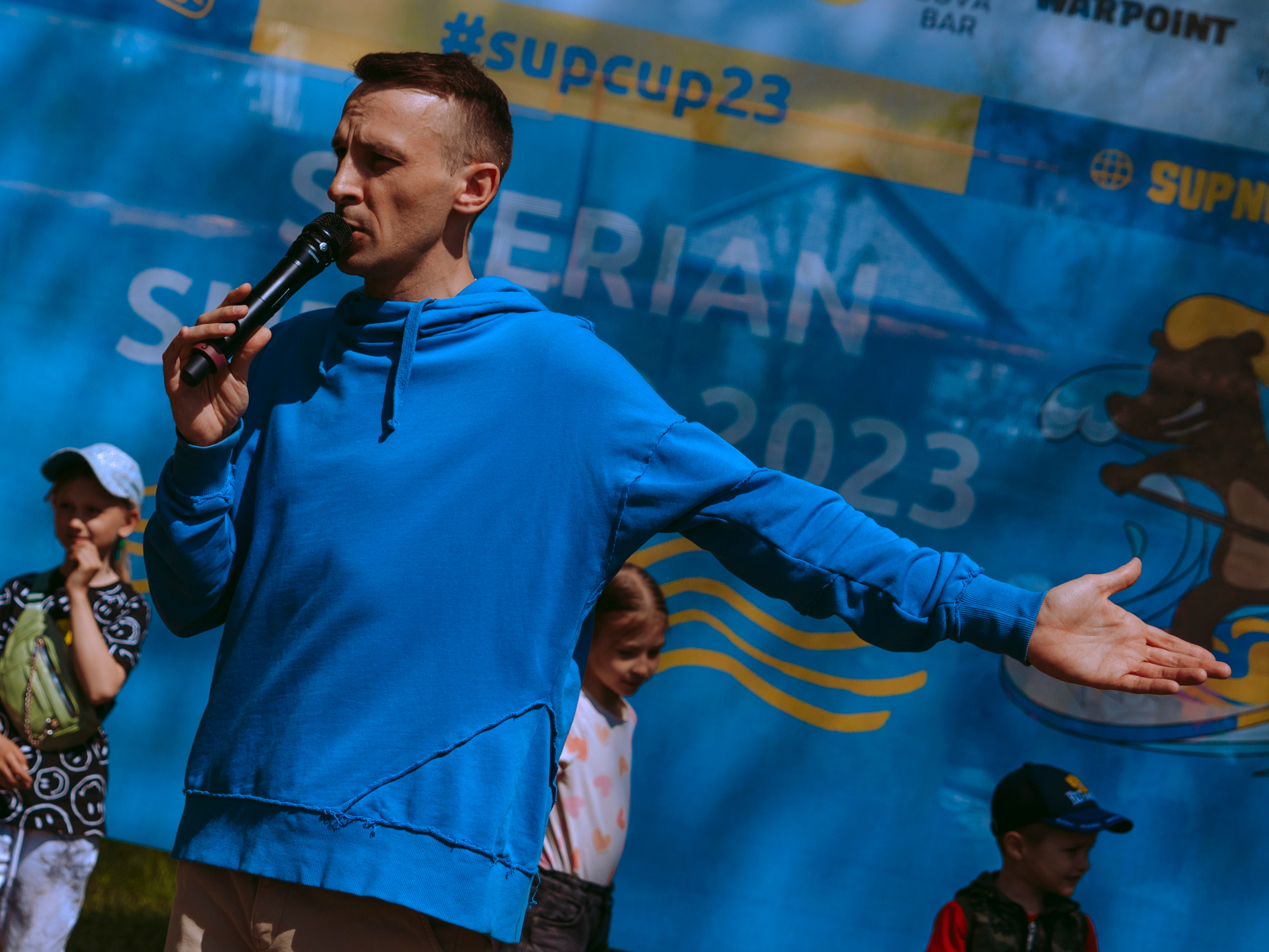 Ведущий разводит руками и говорит в микрофон.