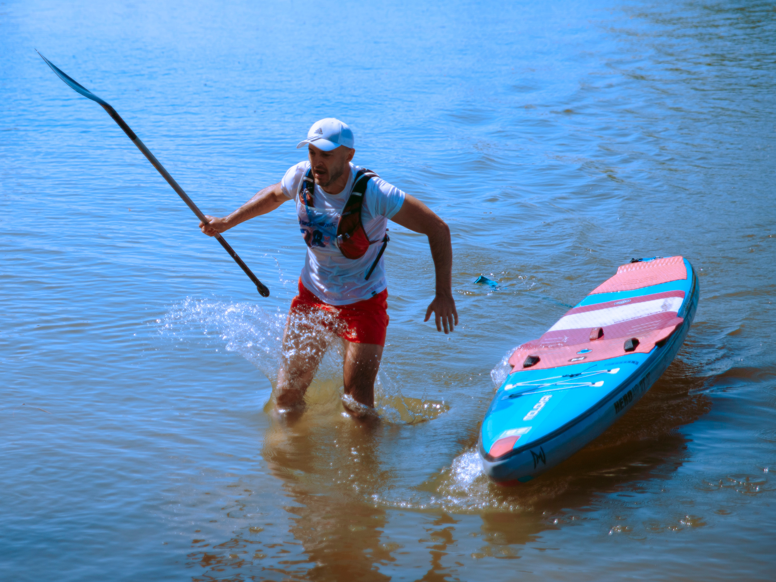 Мужчина спрыгивает с сапа в воду и бежит к берегу.