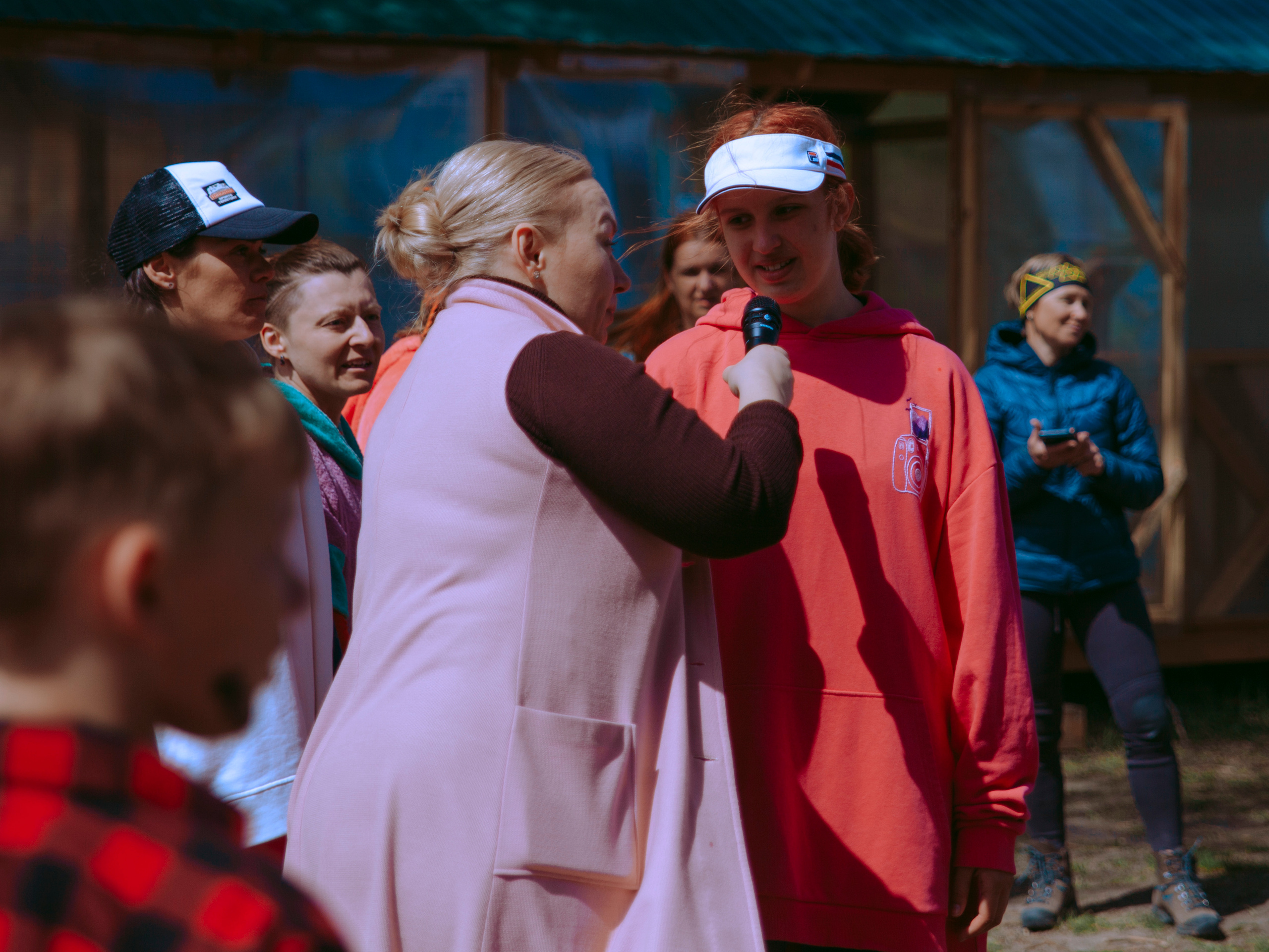 Женщина подает микрофон девочке в кепке.