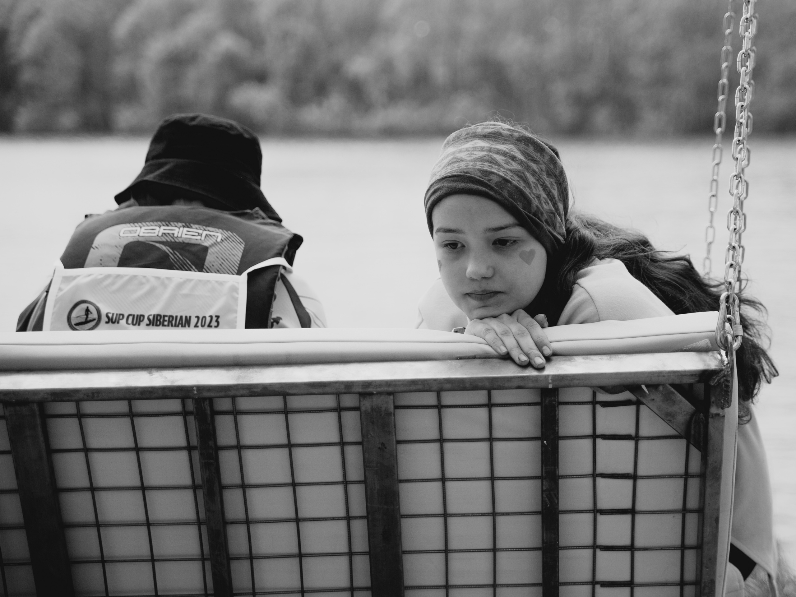 Девочка подросток сидит на качелях на фоне воды, чб фото.
