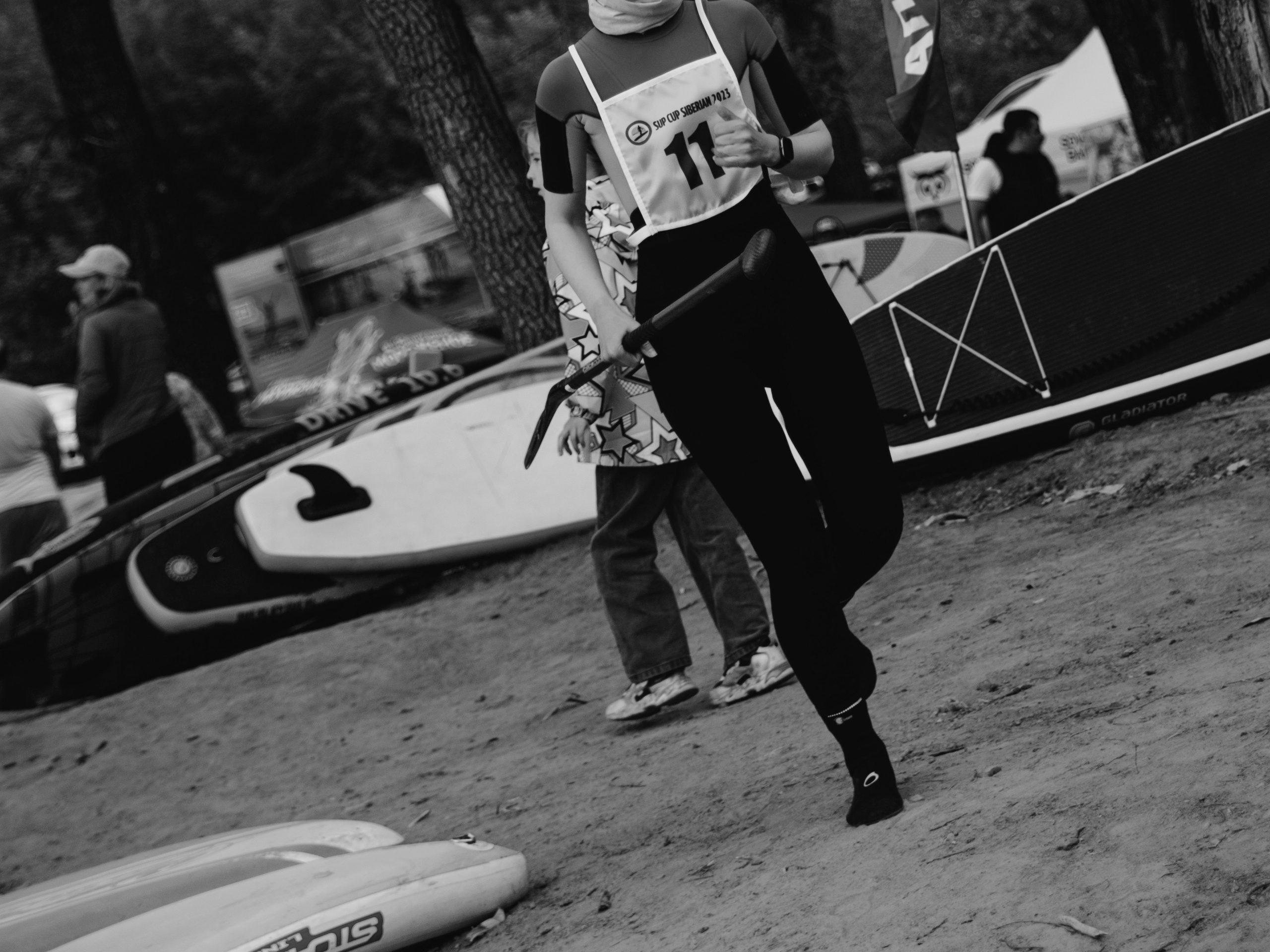 Девушка спортсменка с порядковым номером на груди бежит по берегу на фоне сапов.