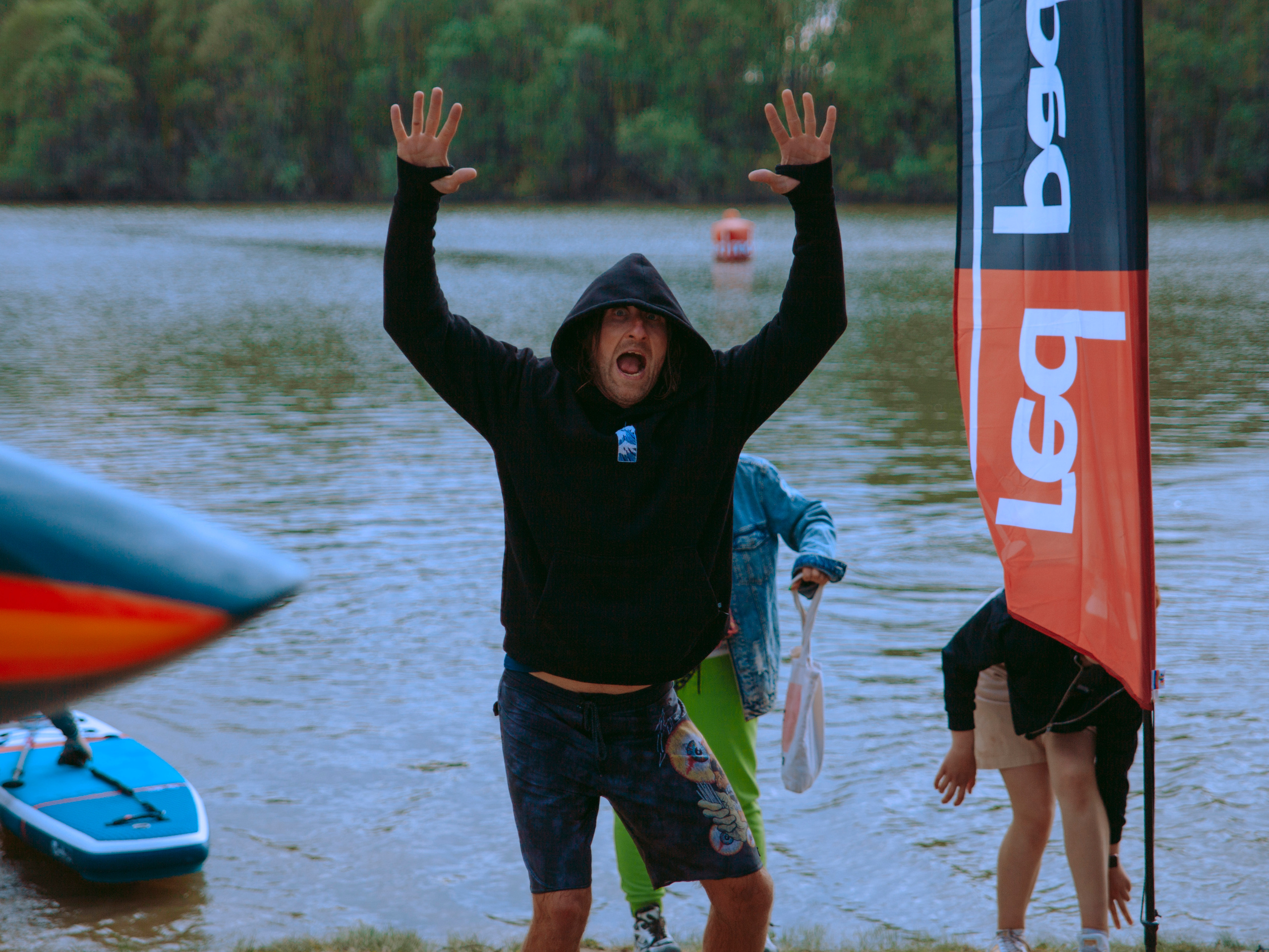 Мужчина в капюшоне поднимает руки и кричит, позирует на камеру.