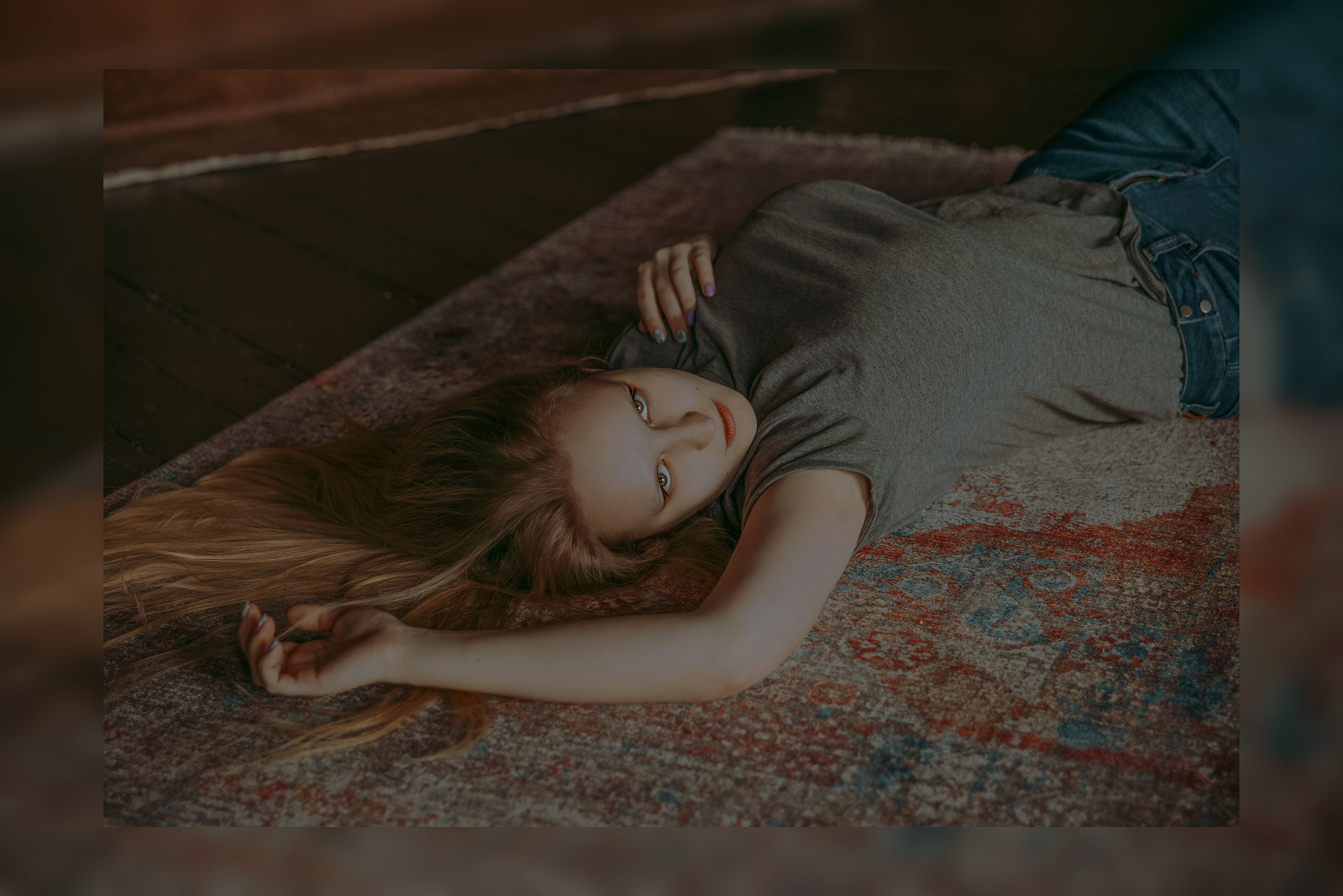 Девушка в серой футболке лежит на узорном ковре с необычным принтом.