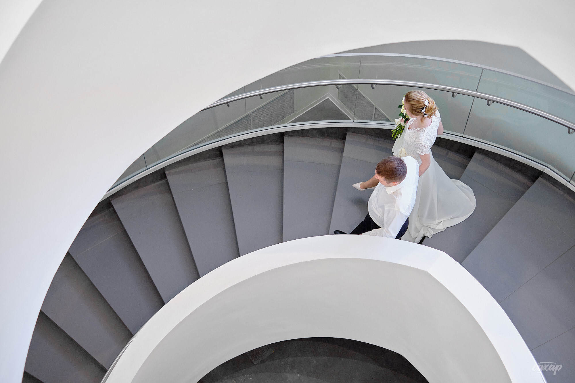 жених и невеста в белом платье спускаются по леснице