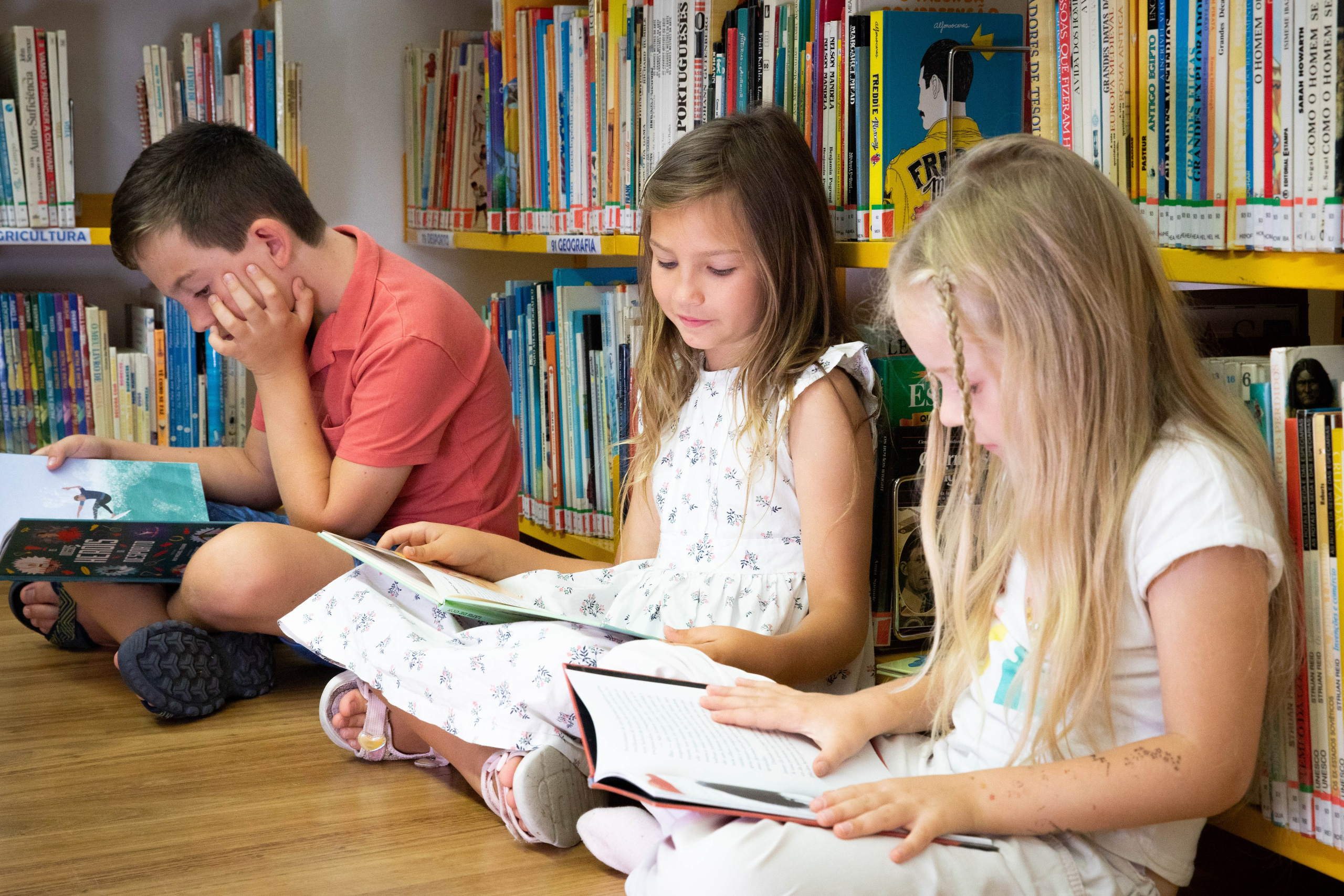 Children immersed in books, sitting together in the library, enjoying a quiet reading moment.