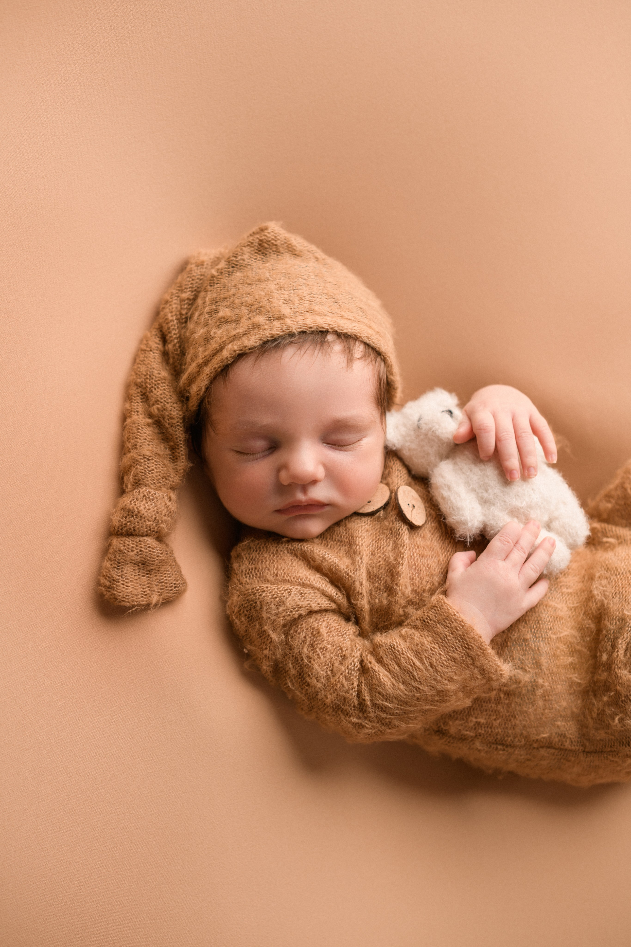 Новорожденный мальчик обнимает маленького белого мишку на однотонном фоне  в детской фотостудии Алёны Лариной "В капусте"