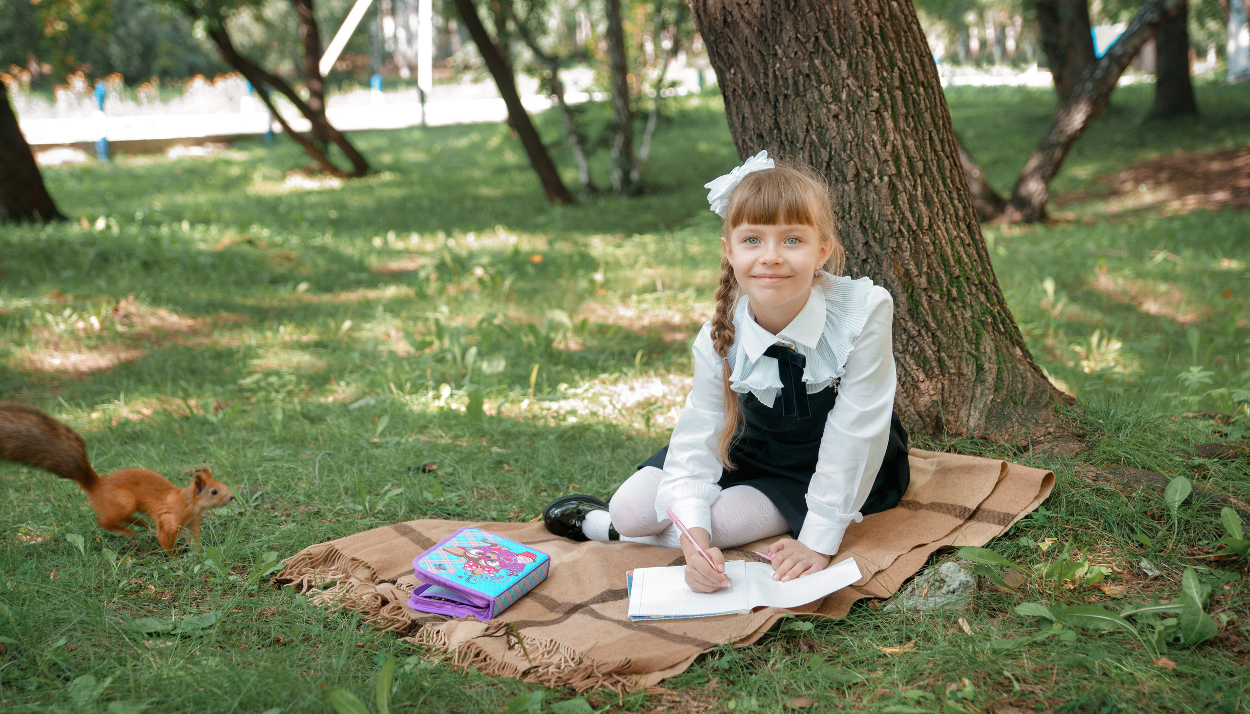 Детская фотосессия осенью - школьница сидя у дерева улыбается