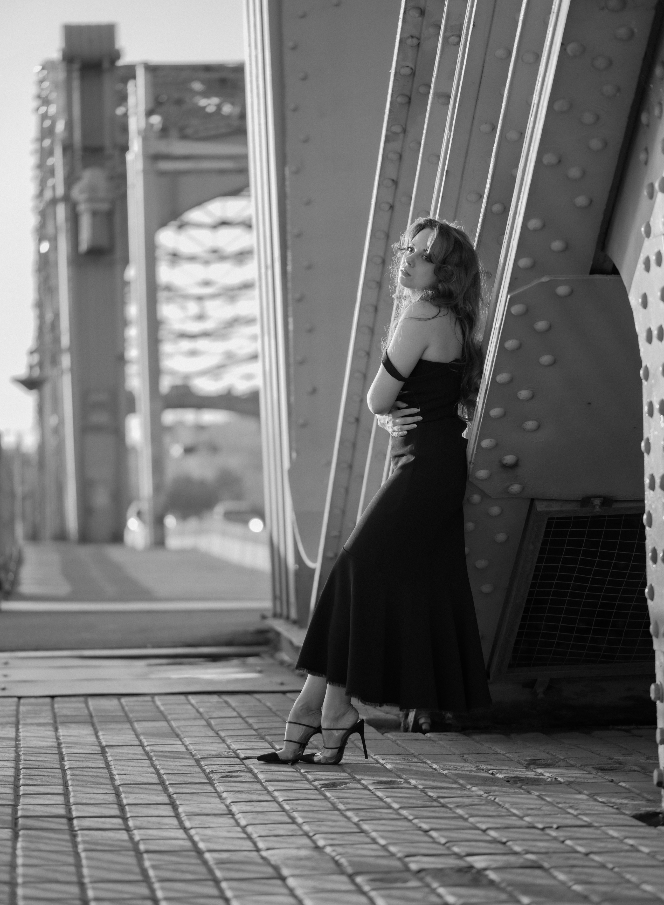 Фотосъемка в Санкт-Петербурге. Белые ночи. Пленэр. Большеохтинский мост. Красивая девушка в черном платье опирается на фермы моста