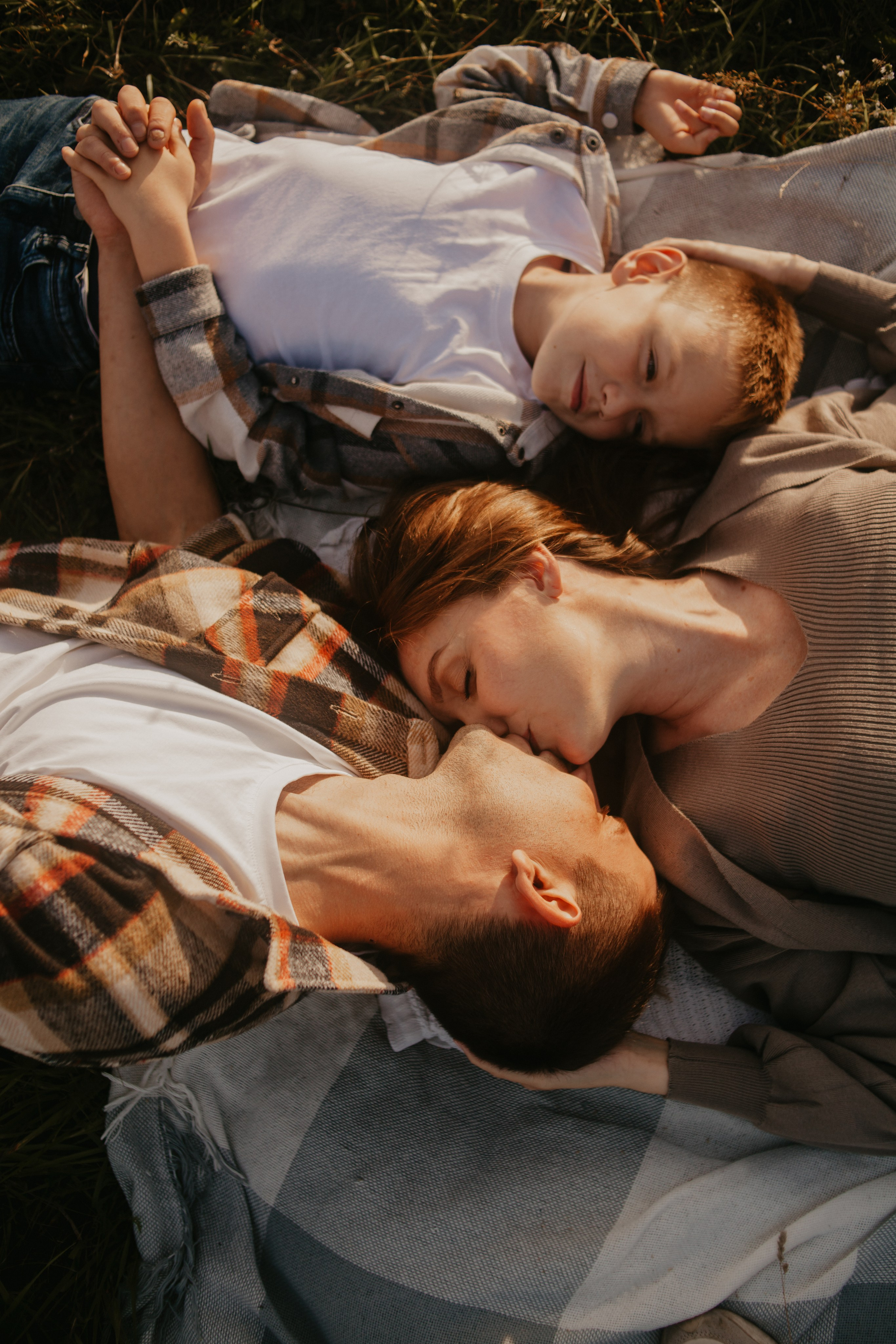 Папа, мама и сын позируют лежа на траве на Колтушских высотах.