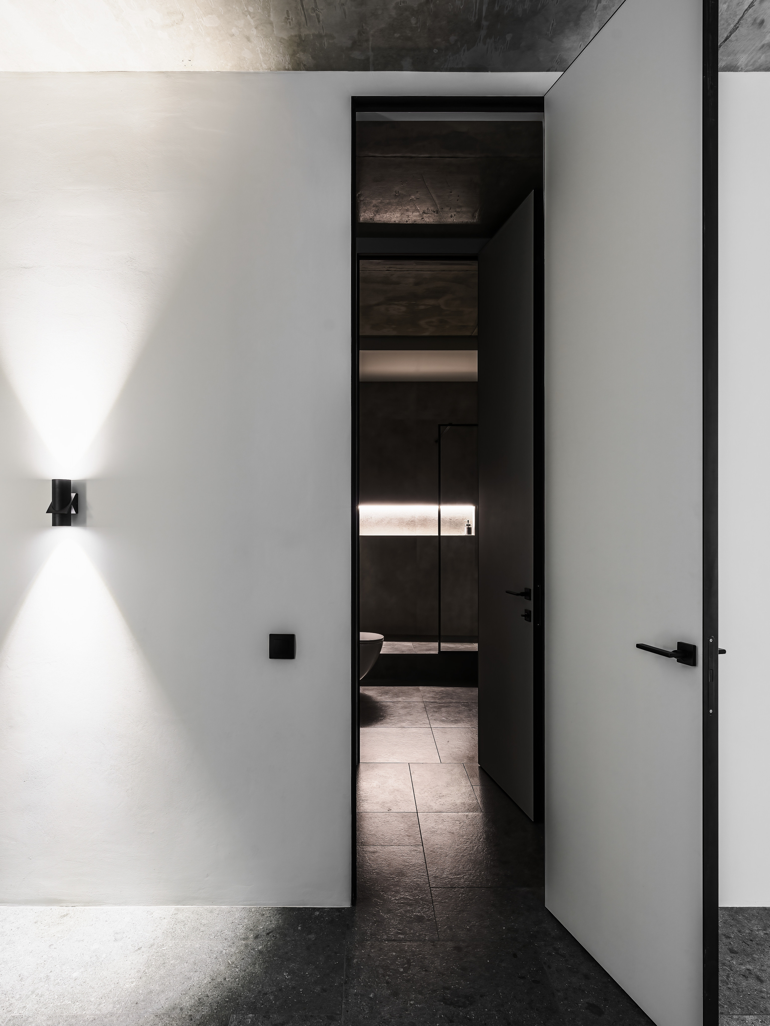 Интерьерный снимок коридора с открытой дверью в ванную комнату, бетонным потолком и контрастным освещением. Авторский дизайн Андрея Нелень и Екатерины Проскуряковой, профессиональная фотосъёмка Сергея Денисенко.