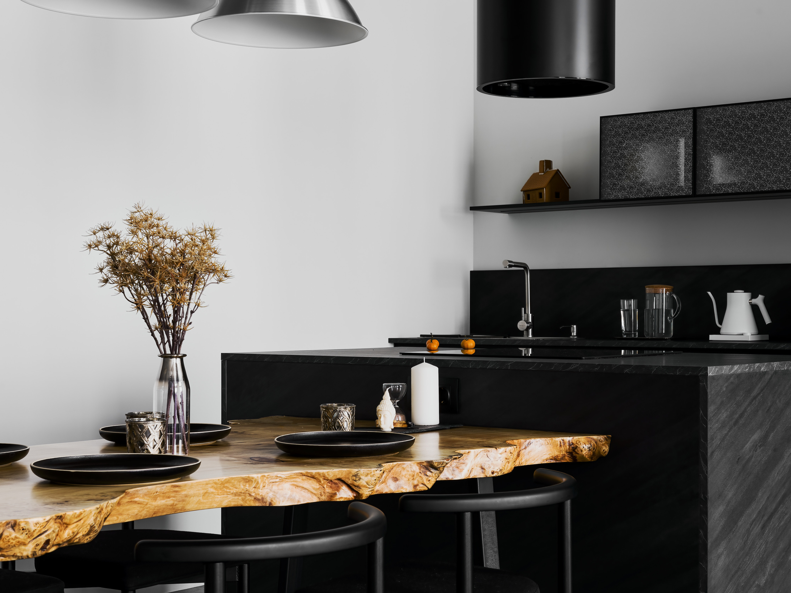 Деталь интерьера кухни-столовой: деревянный обеденный стол с живым краем, чёрные стулья и фон с кухонным гарнитуром из тёмного камня. Авторский дизайн Андрея Нелень и Екатерины Проскуряковой, фотосъёмка Сергей Денисенко.