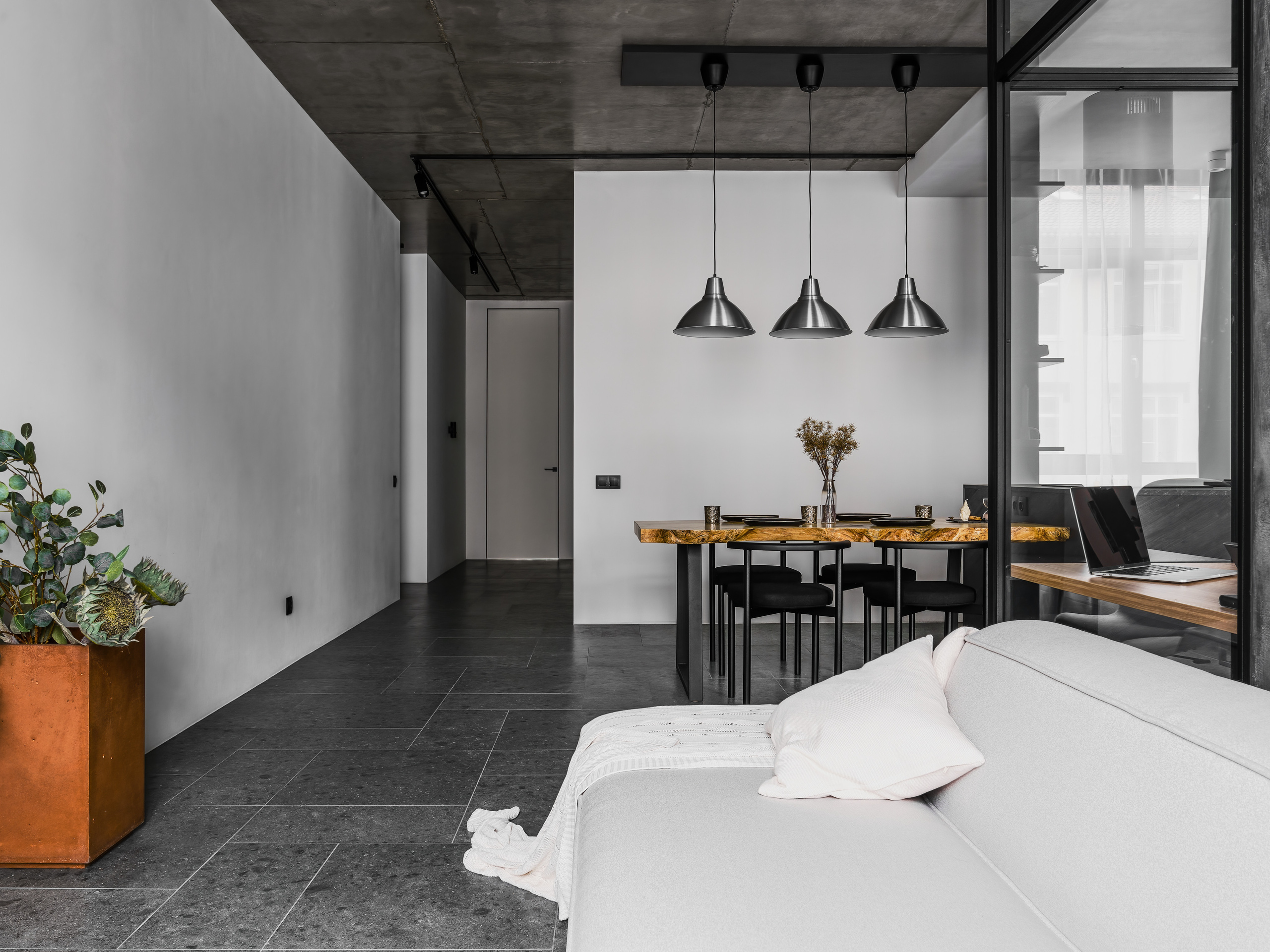 Интерьер гостиной с видом на обеденную зону: деревянный стол из массива с живым краем, три подвесных светильника и бетонный потолок. Проект дизайнеров Андрея Нелень и Екатерины Проскуряковой, фотограф Сергей Денисенко.