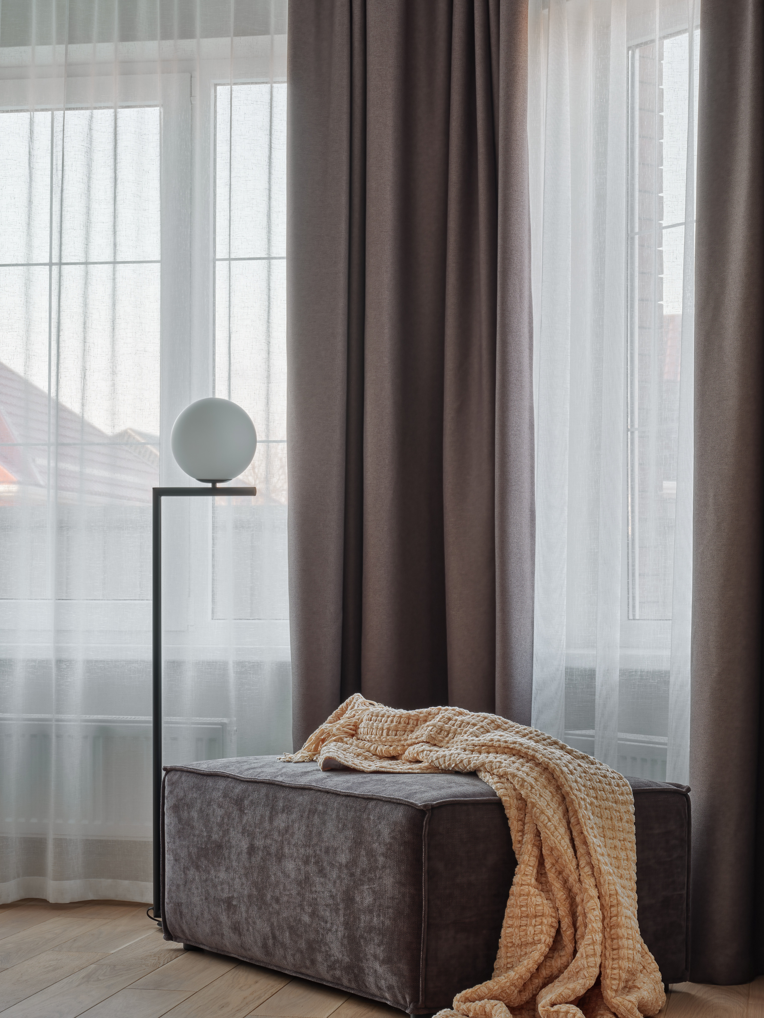 Уютный уголок у окна с серым пуфом, бежевым пледом, плотными шторами и торшером в минималистичном стиле. Интерьер оформлен дизайнером Анжеликой Исаевой, профессиональная фотосессия Сергея Денисенко.