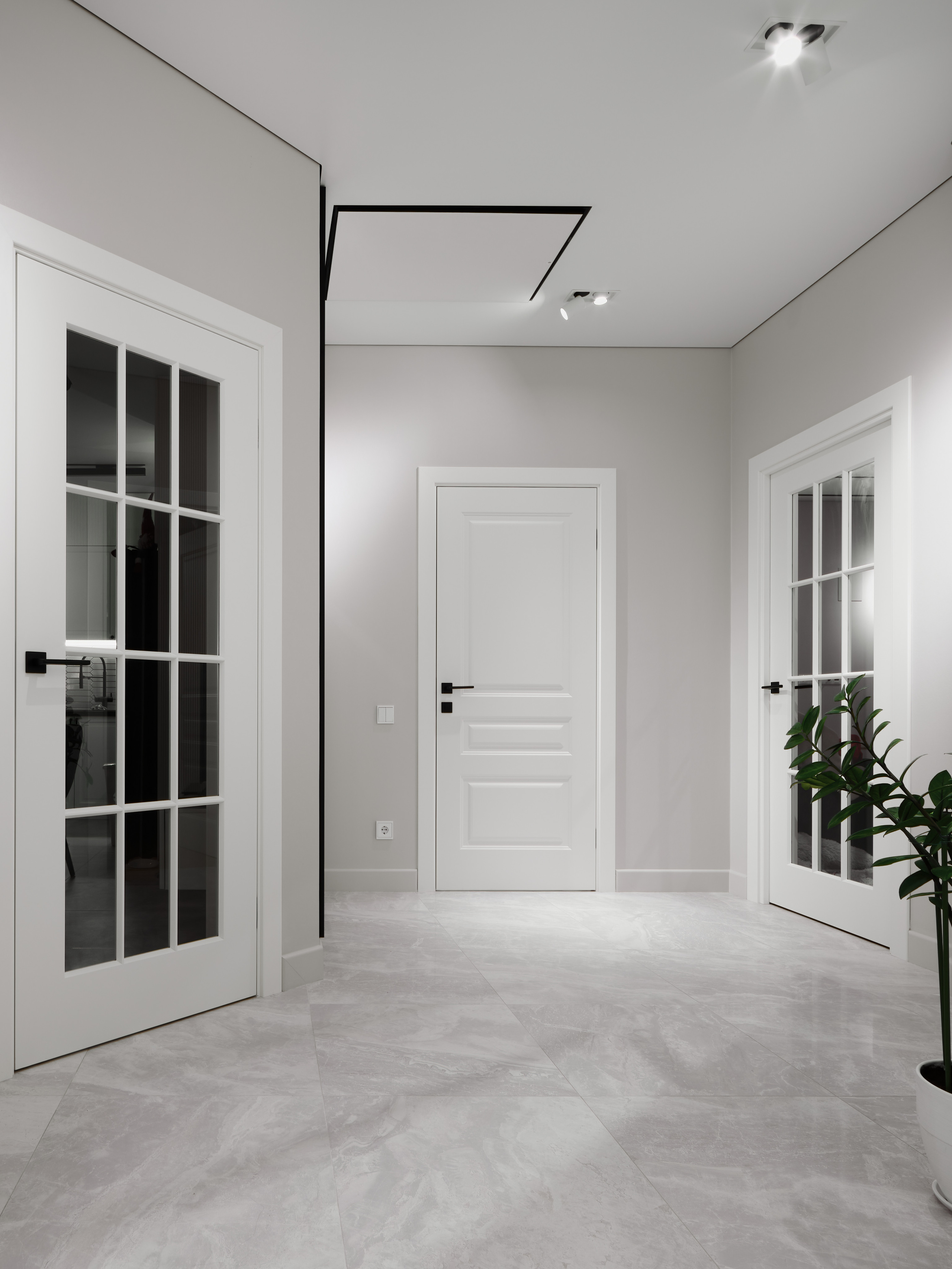 Светлый коридор с тремя белыми дверями, встроенными светильниками и акцентом на строгие черные ручки. Пространство оформлено в стиле минимализм. Дизайн Анжелика Исаева, профессиональная интерьерная съемка Сергей Денисенко.