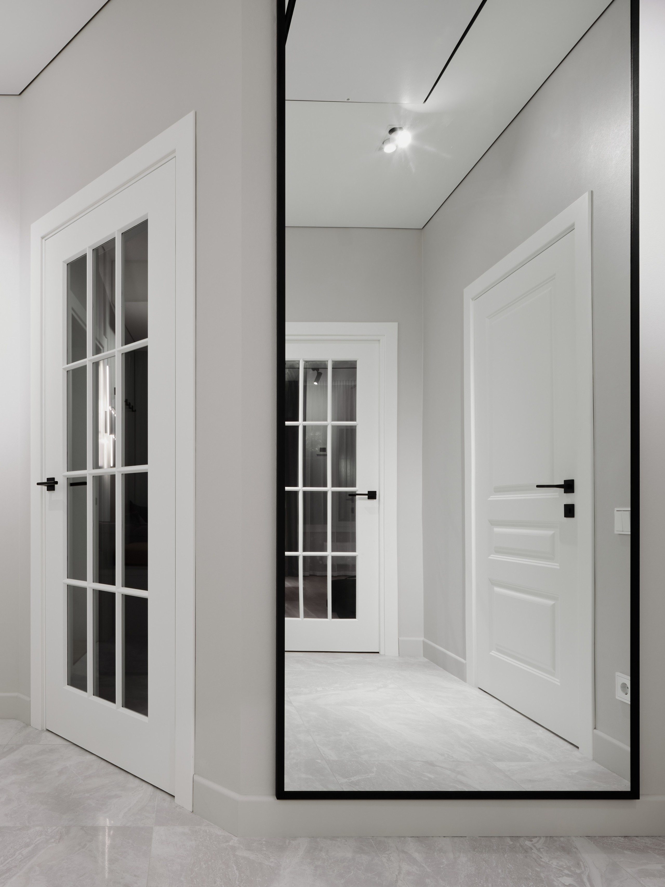Современный минималистичный интерьер прихожей с белыми дверями со стеклянными вставками, большим зеркалом в черной раме и светлым мраморным полом. Автор дизайна Анжелика Исаева, интерьерная фотосъемка Сергей Денисенко.