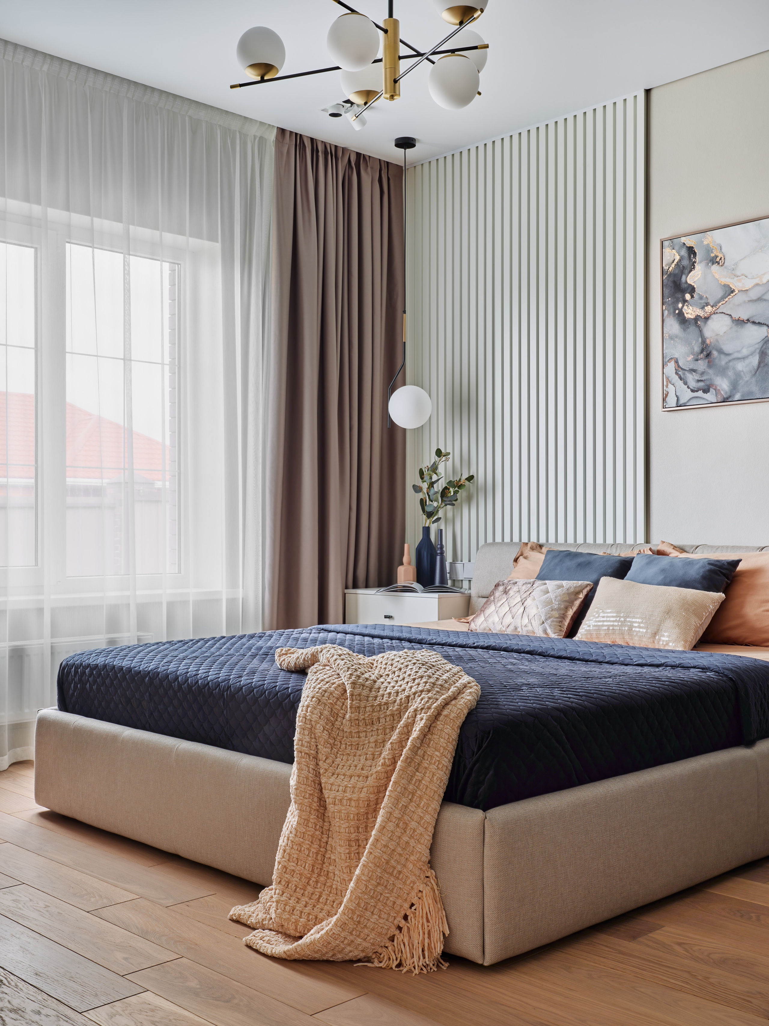 Просторная современная спальня с большой кроватью, мягким изголовьем, темно-синим покрывалом, декоративными подушками и современным светильником. Дизайнер Анжелика Исаева, фотограф Сергей Денисенко.