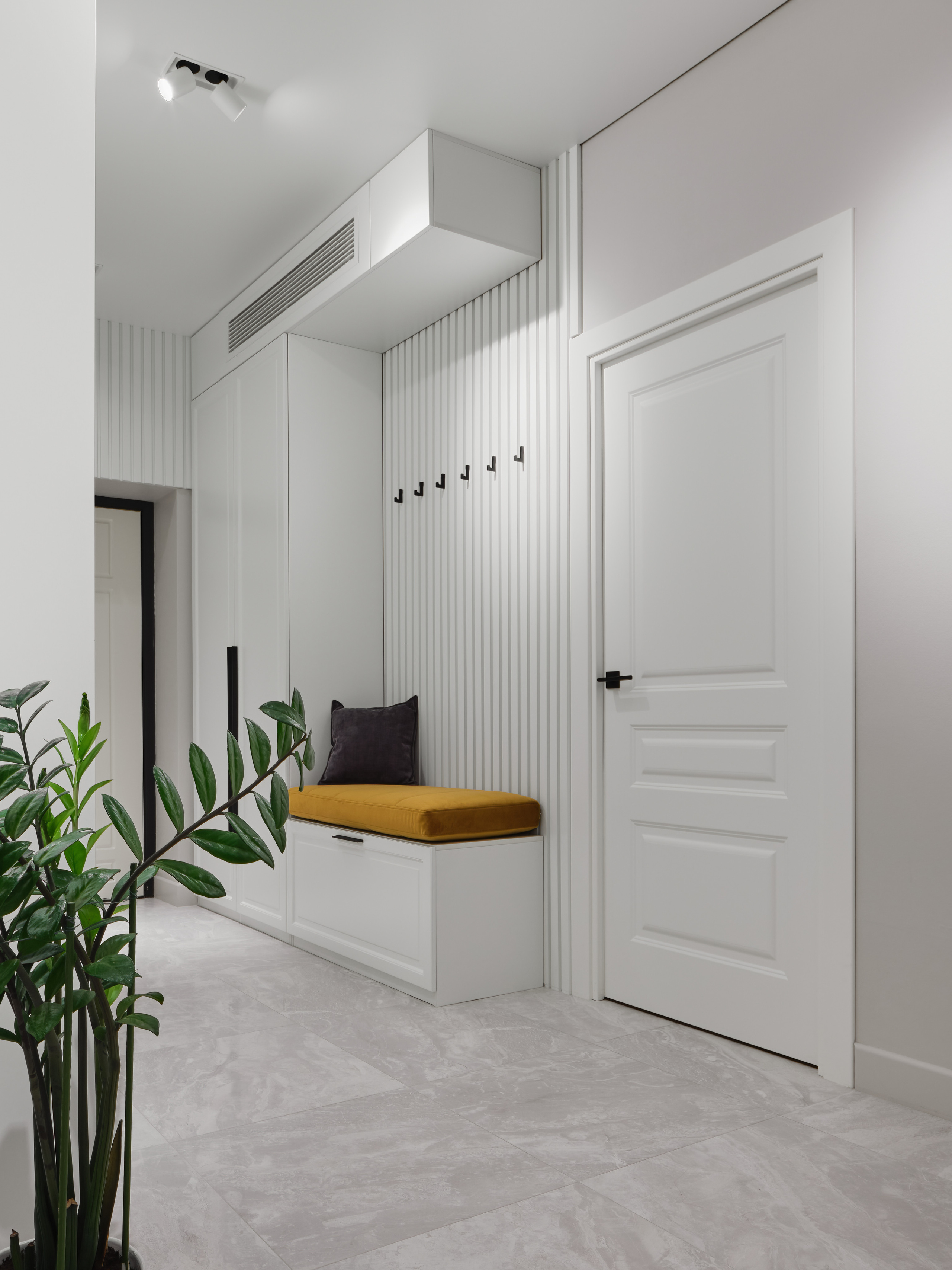 Функциональная зона прихожей с мягкой скамьей с горчичной подушкой, белым шкафом и вертикальными панелями на стене. Стильный современный интерьер от дизайнера Анжелики Исаевой, съемка выполнена Сергеем Денисенко.