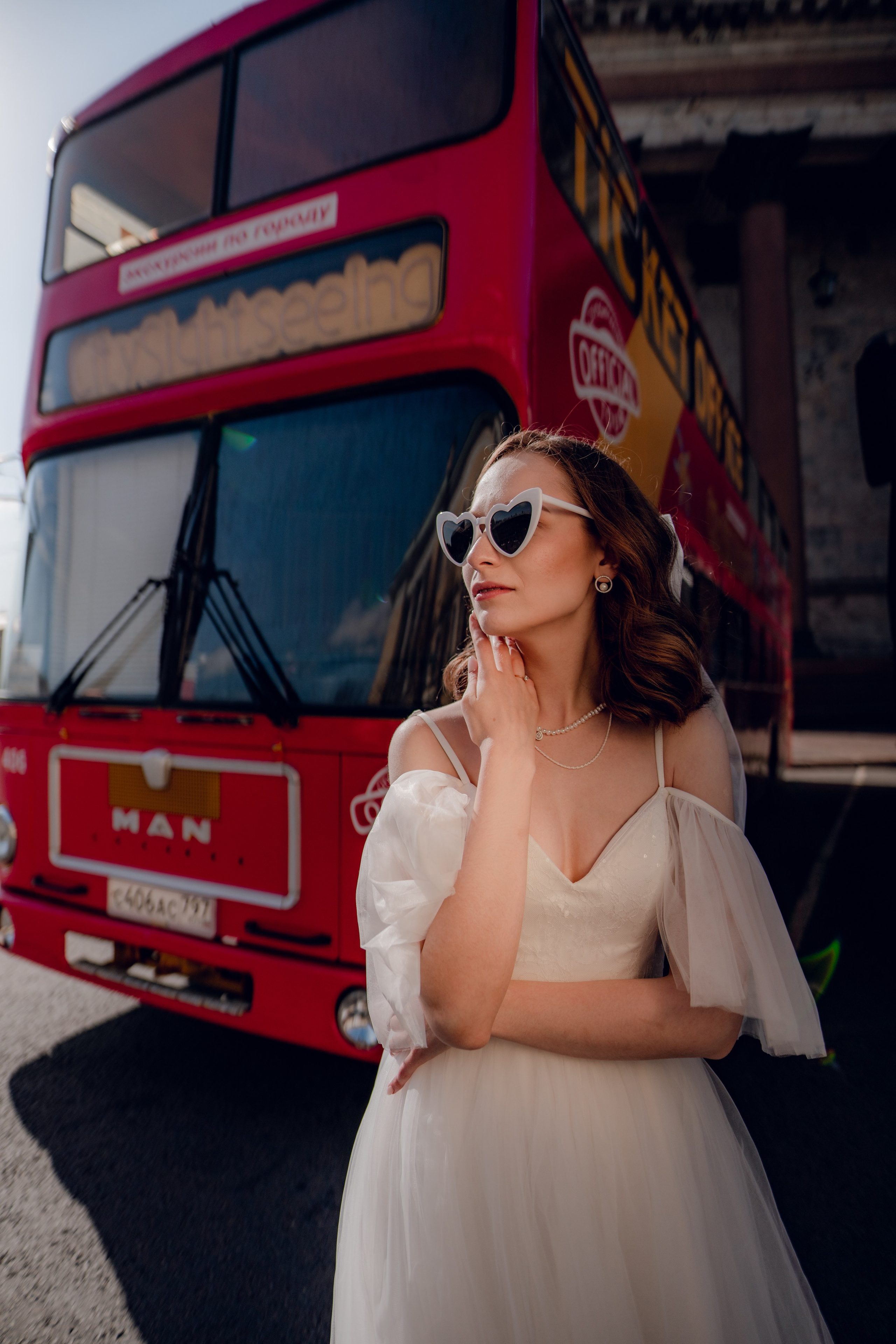 невеста в солнечных очках стоит около красного туристического автобуса