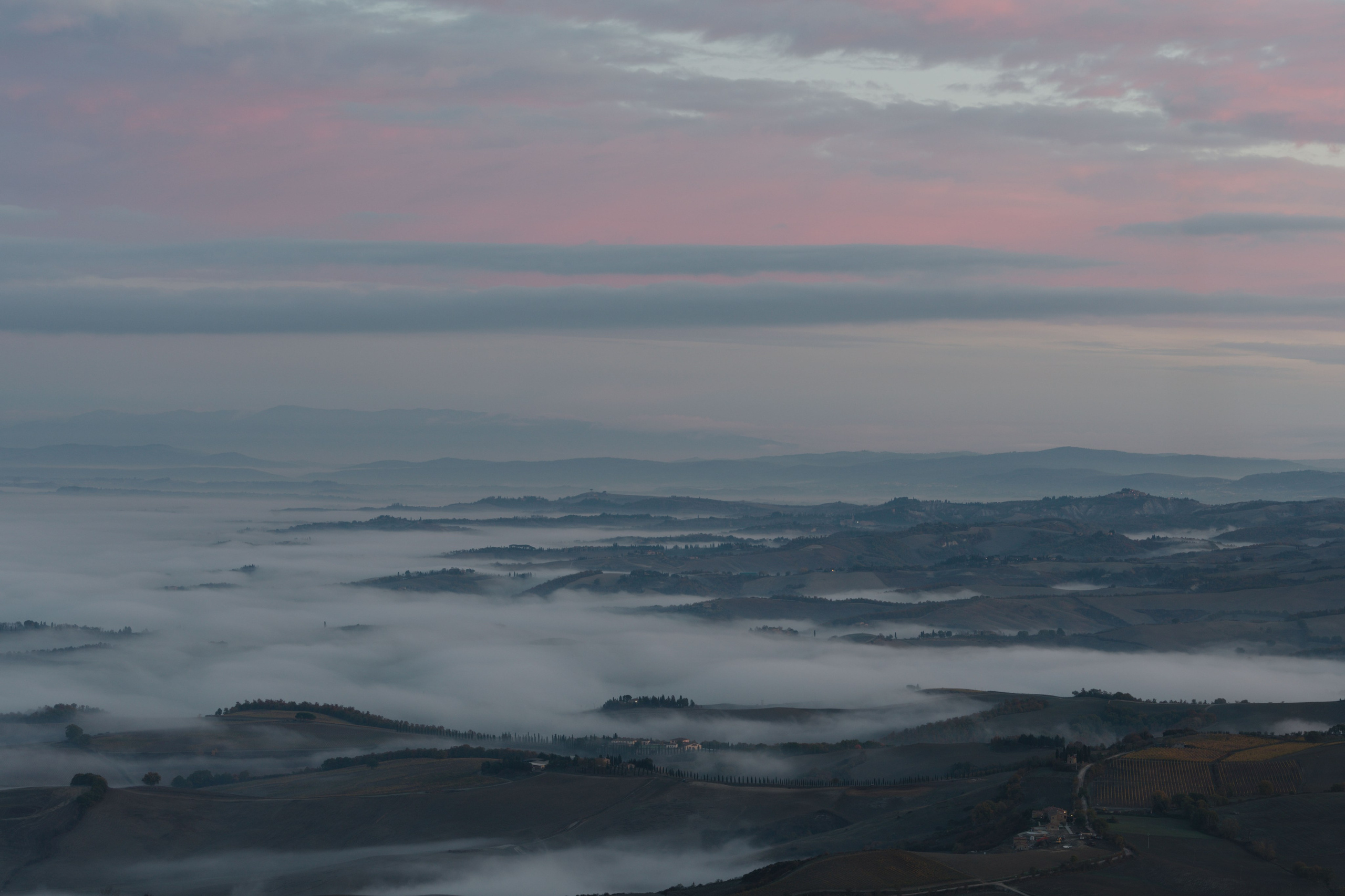 Атмосферный пейзаж Тосканы на рассвете: туман стелется по долинам между холмами, создавая многослойный эффект.