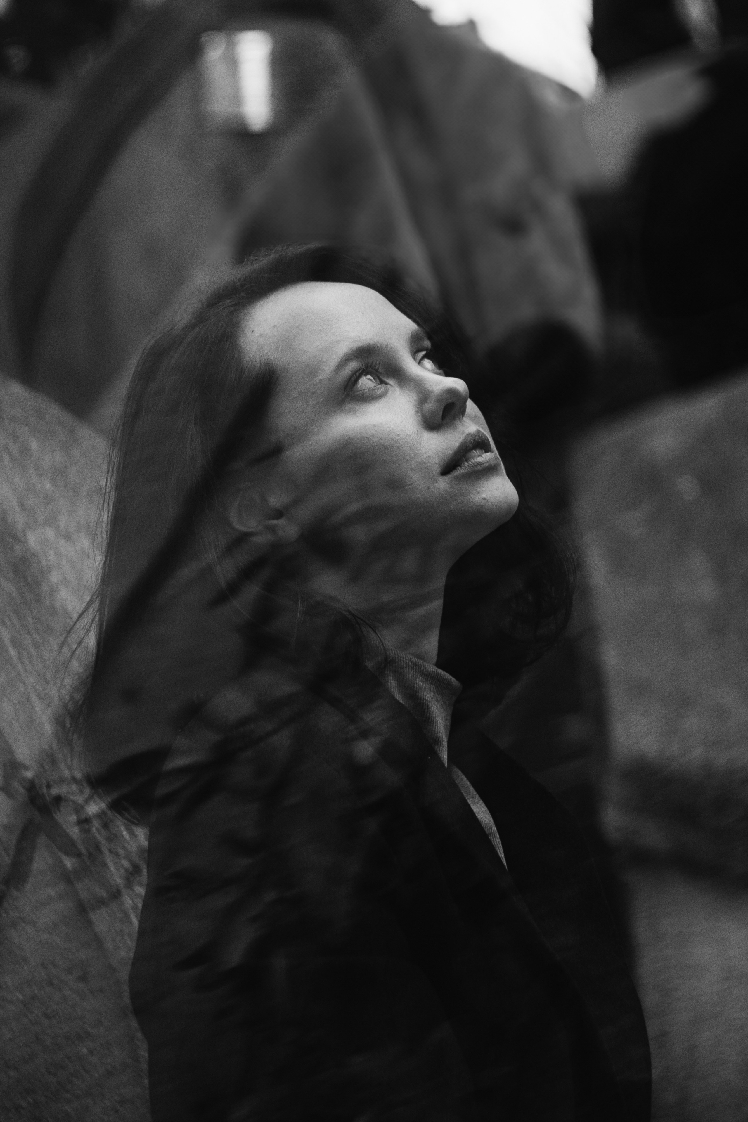 Черно-белая фотография с двойной экспозицией изображающая девушку, смотрящую наверх и стоящую боком к нам. На изображение девушки наложено изображение веток деревьев