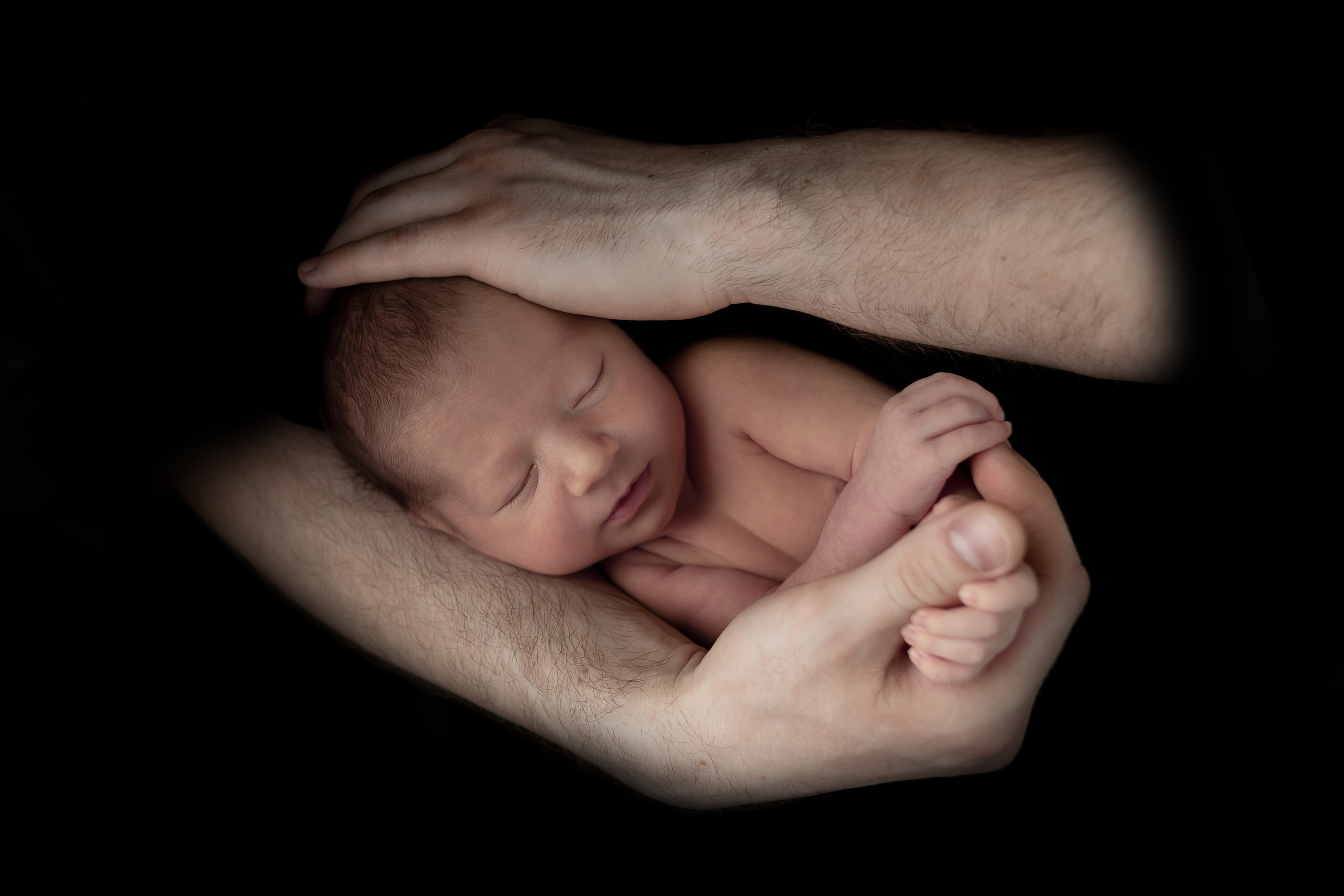 Отец держит спящего младенца на черном фоне