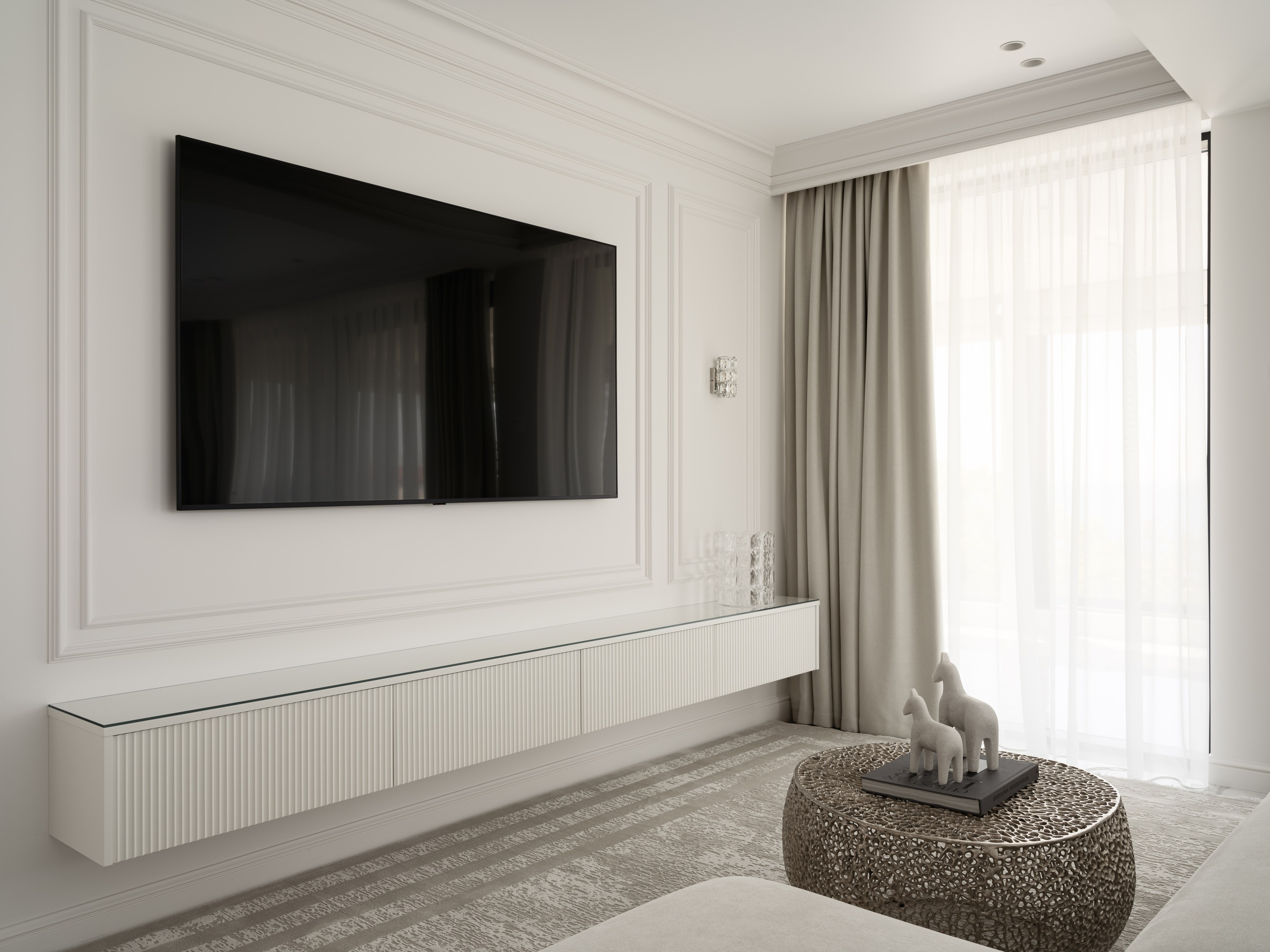 Современная гостиная в светлых тонах с минималистичным настенным телевизором, подвесной консолью и изящным декором — интерьер от дизайнера Алёны Боярской, стилист Наталья Якушева, фотограф Сергей Денисенко, вид в дневном освещении.