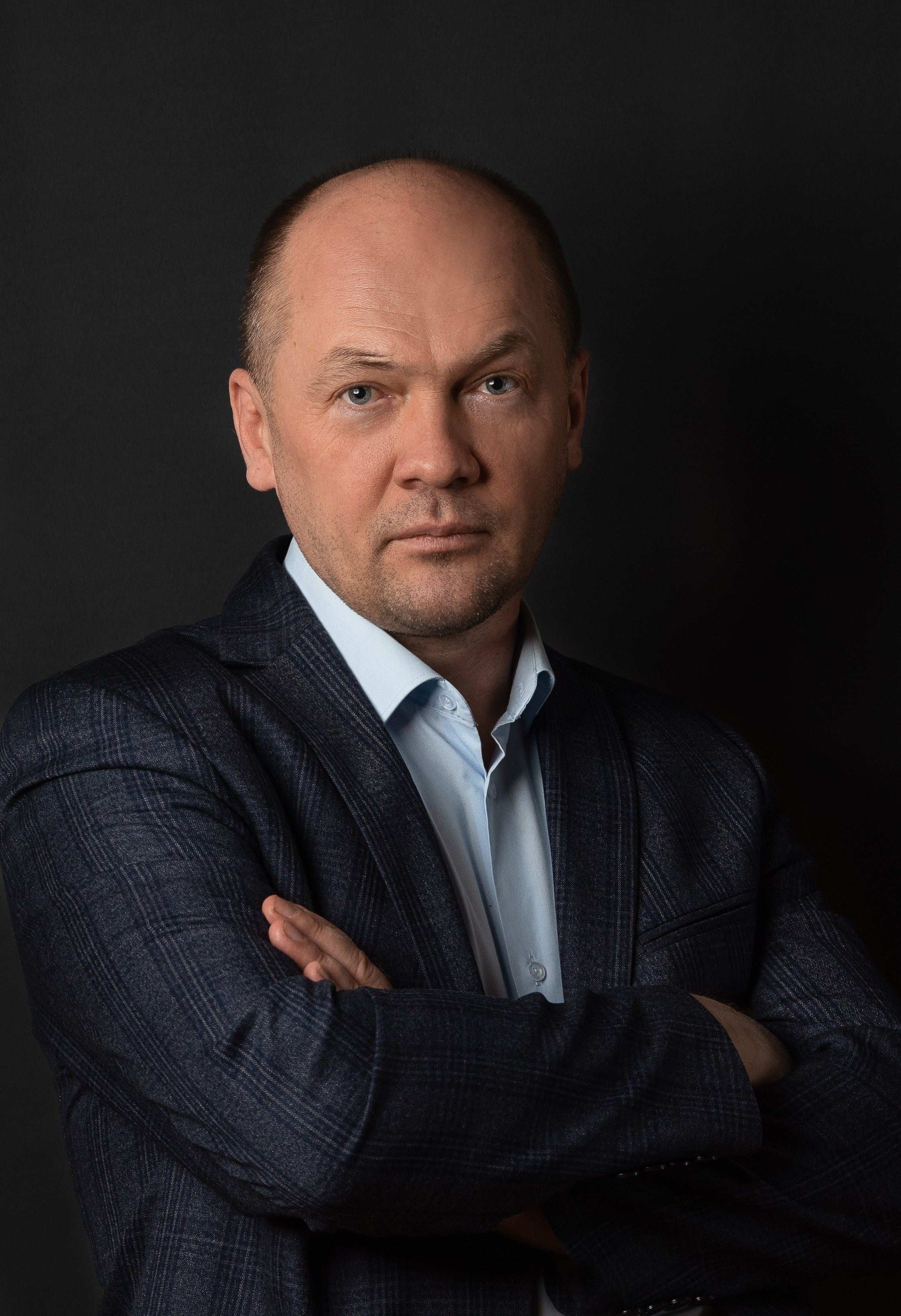 Деловой портрет. Мужчина в классическом костюме стоит скрестив руки на груди и смотрит в объектив камеры