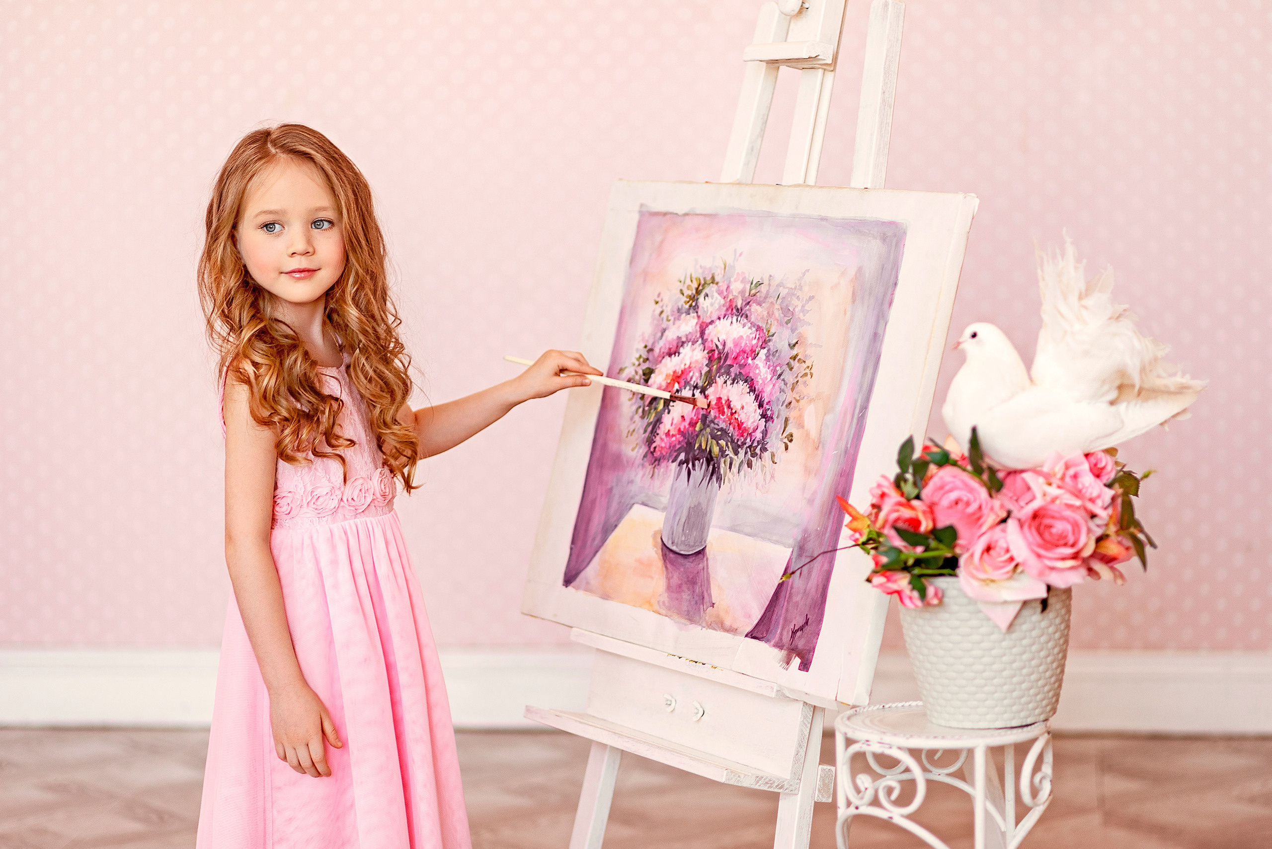 Девочка с кисточкой в руках пишет картину с цветочным натюрмортом.