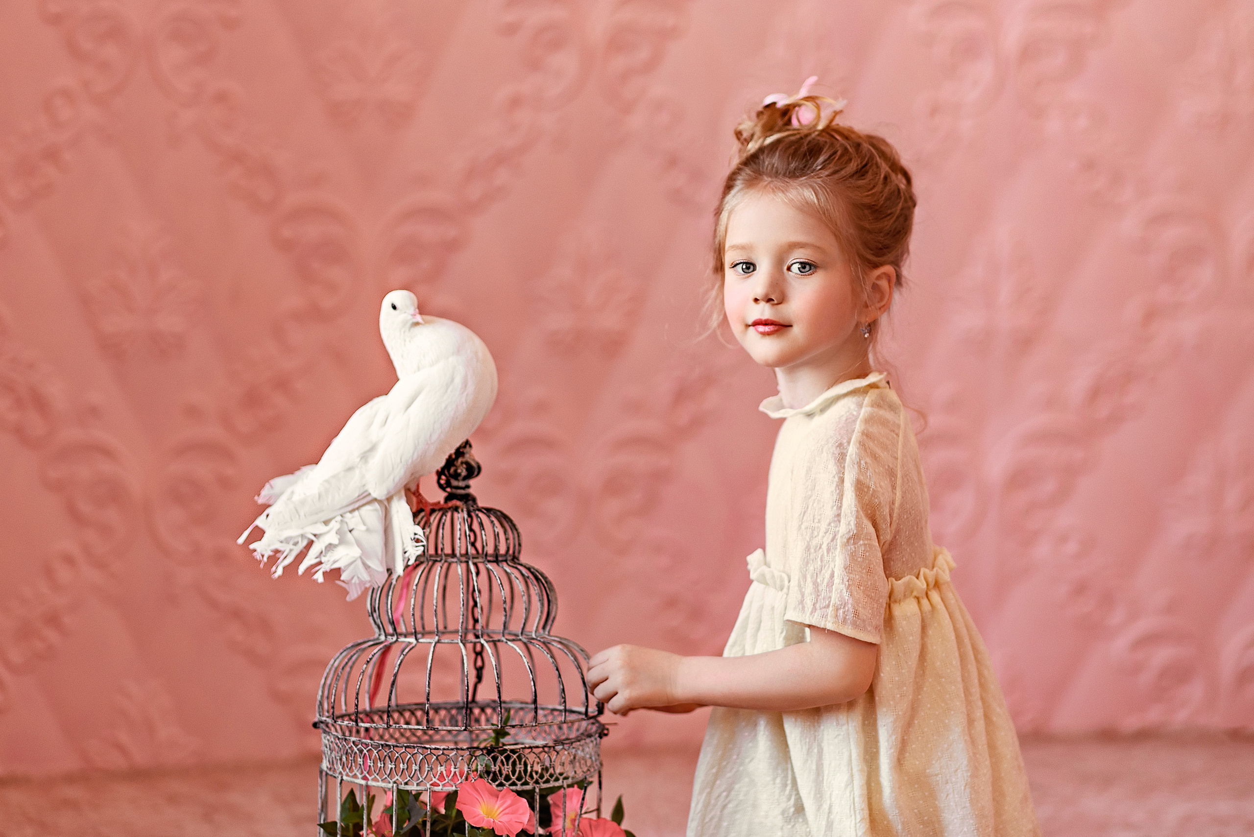 Девочка дотронулась до клетки, на которой сидит белый голубь.